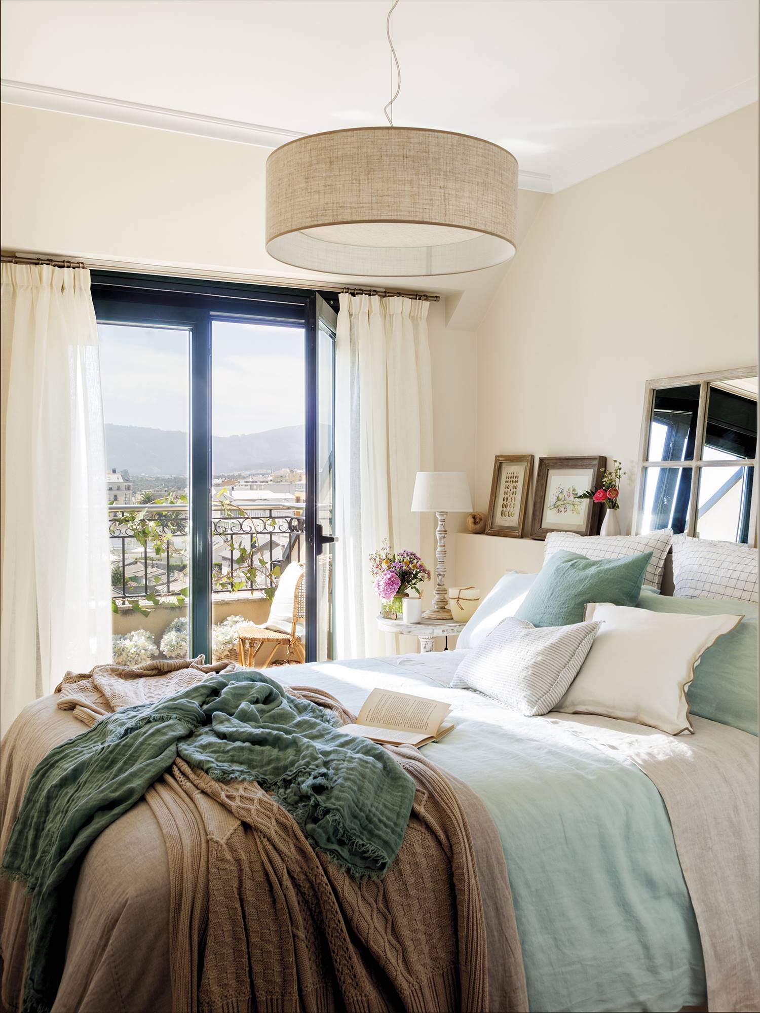 Dormitorio principal en tonos claros y azules con espejo y pequeños cuadros sobre el cabecero