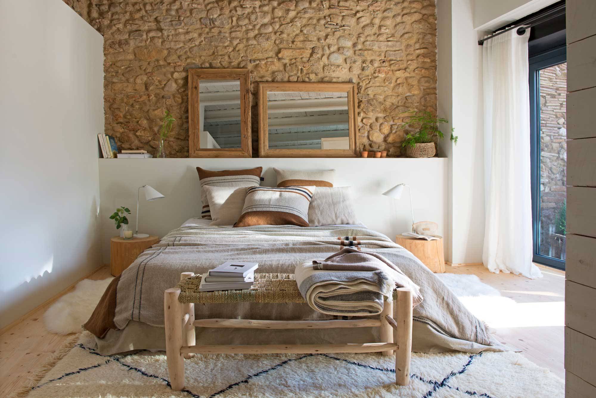 Dormitorio moderno con pared de piedra y espejos sobre el cabecero