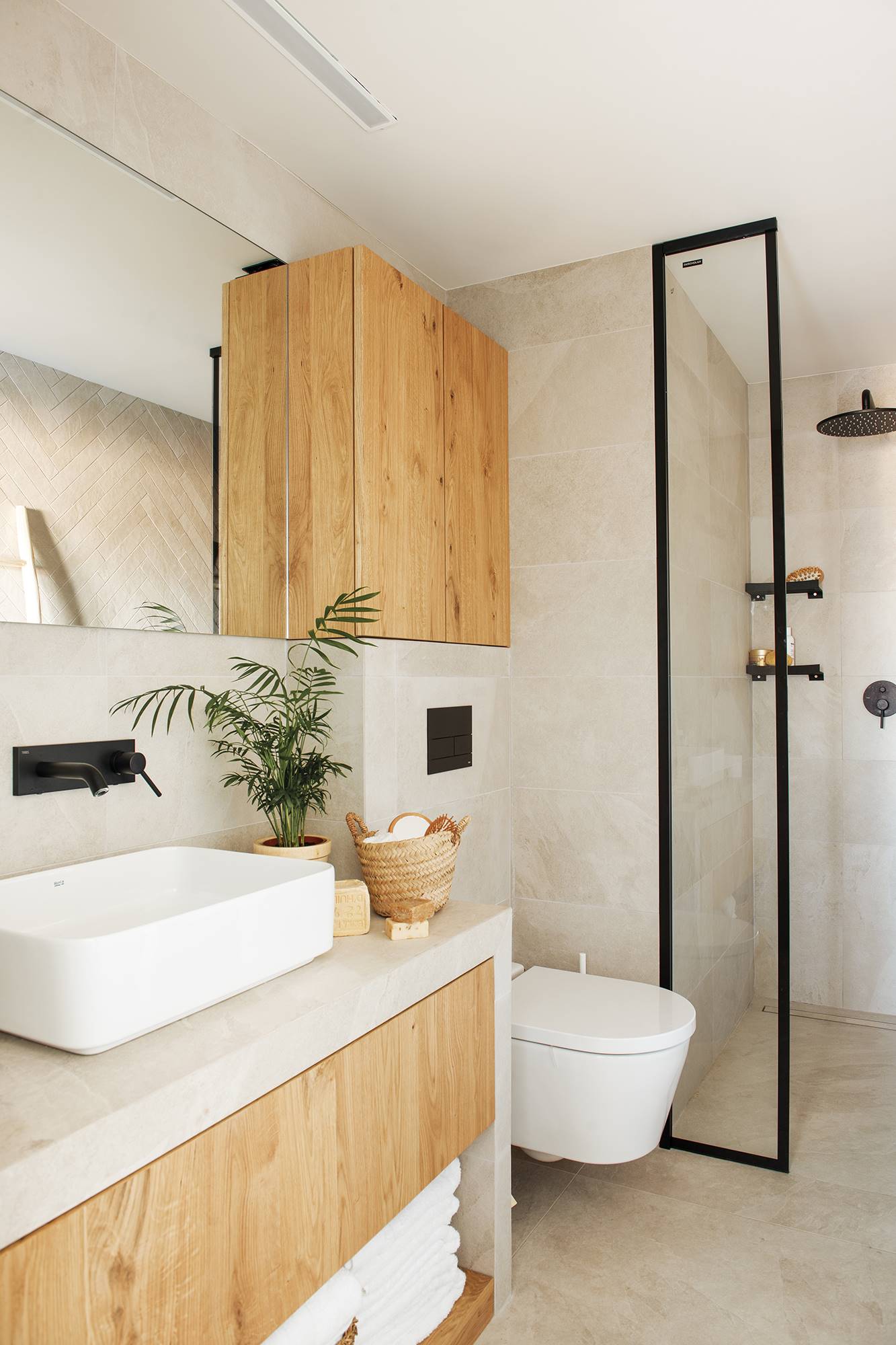 Baño con mueble de baño a medida y puertas de madera y mampara fija con perfiles negros. 