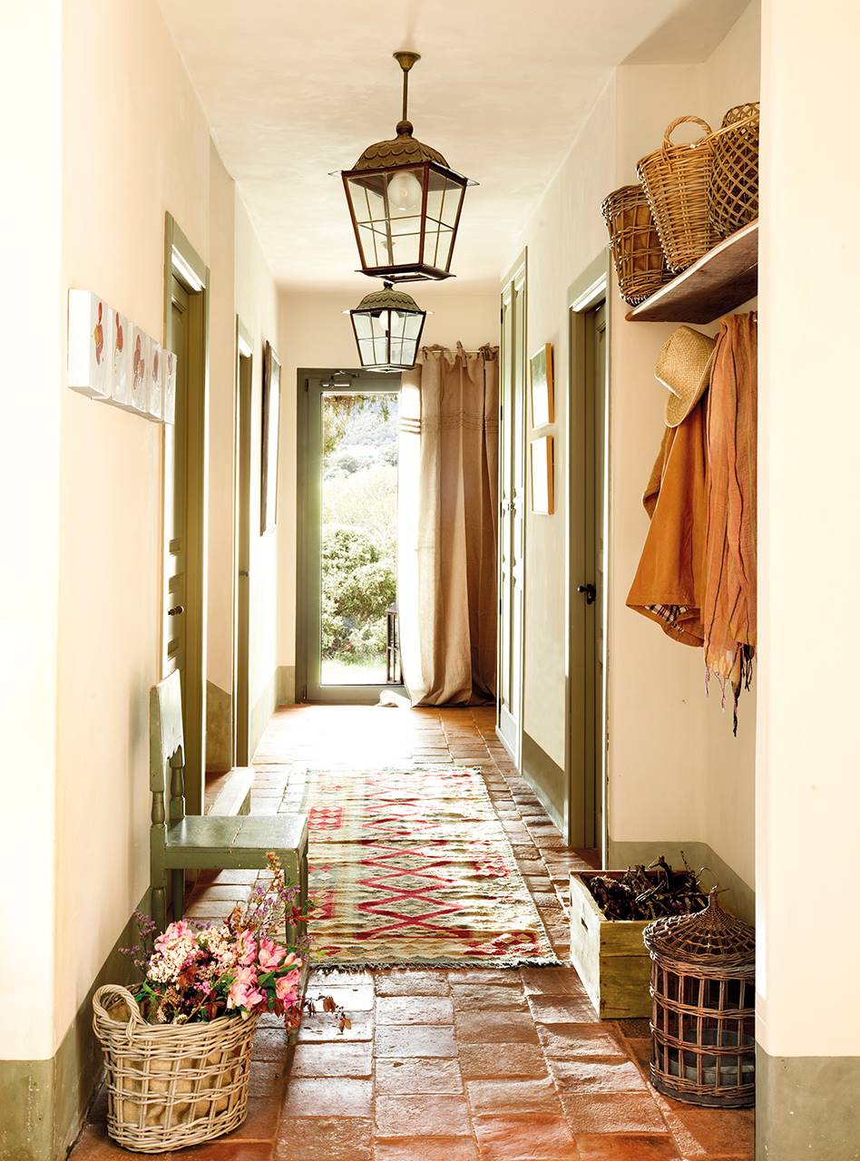 Pasillo de casa campestre con las carpinterías en color verde y suelos de barro. 