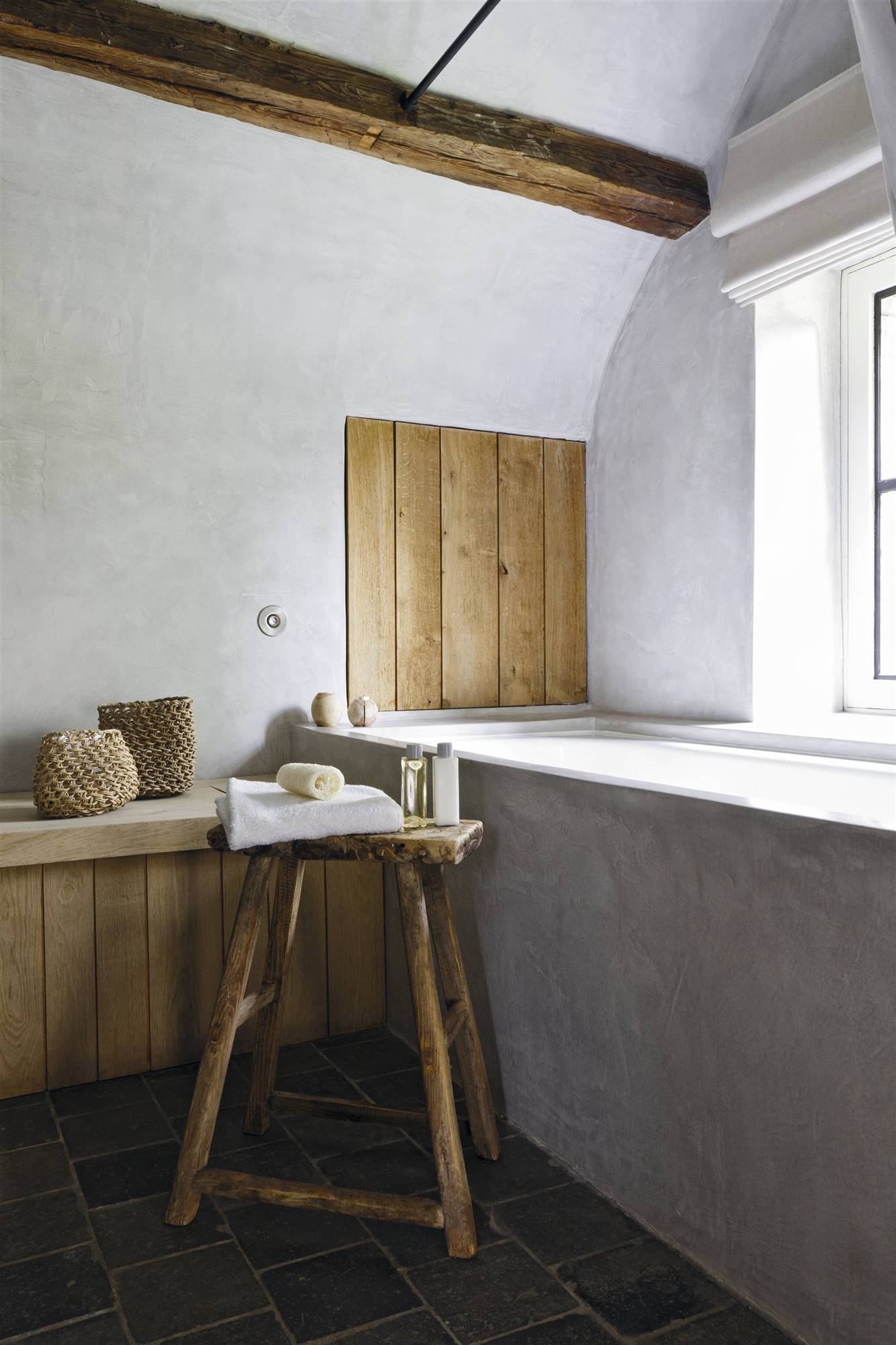 Baño con bañera de cemento y taburete de madera raw