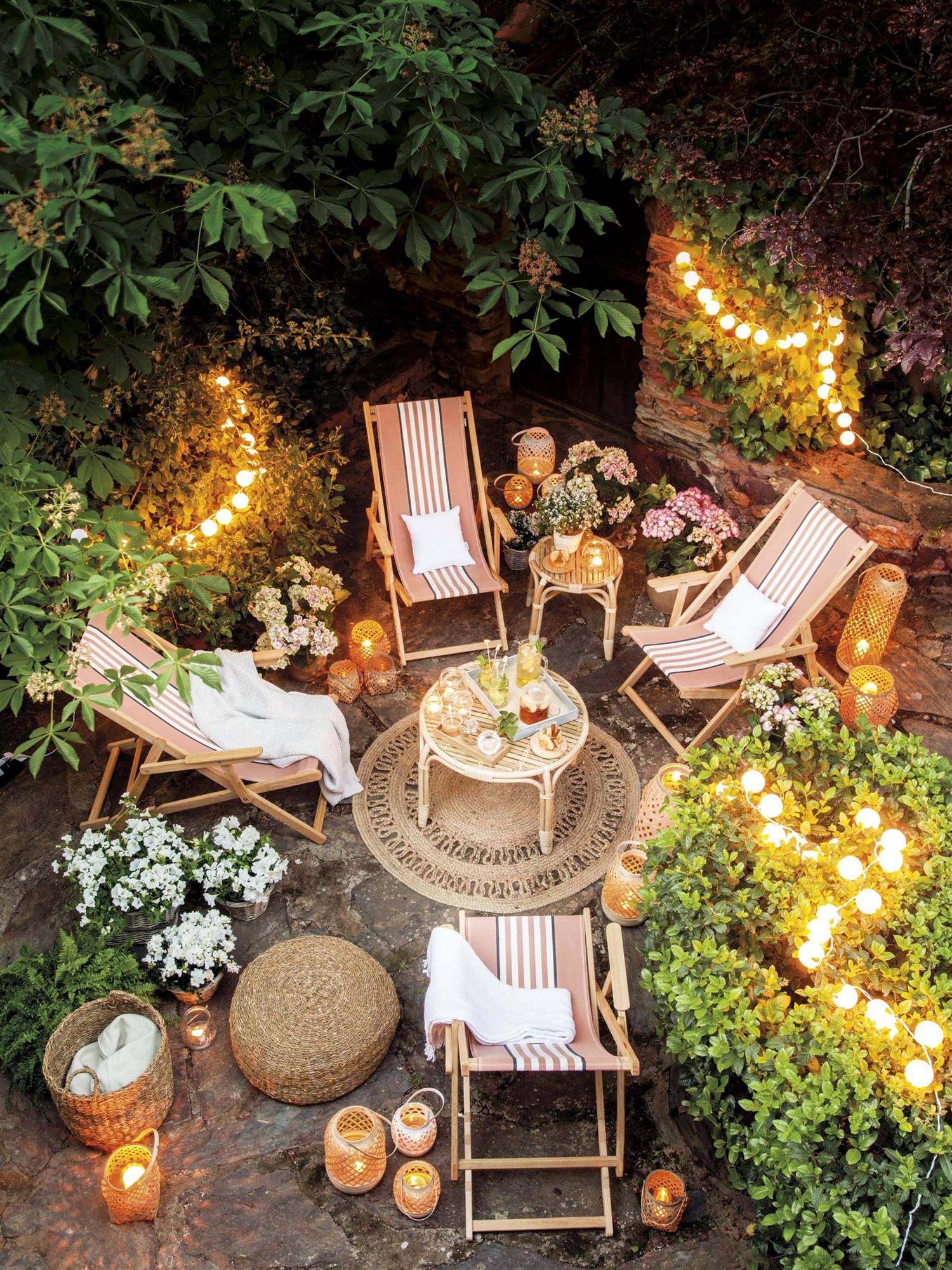 Patio decorado con tumbonas, rodeado de plantas y con guirnaldas de luces.  