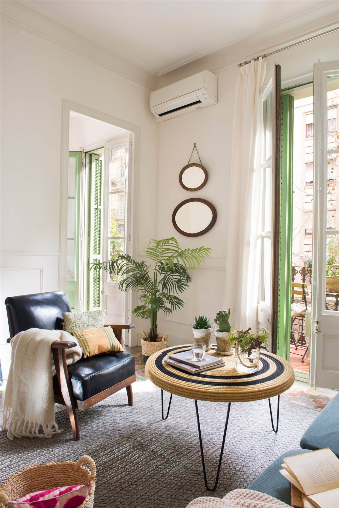 Salón con espejos colgados en la pared y sillón de piel negro con mesa de centro de fibras naturales redonda sobre alfombra