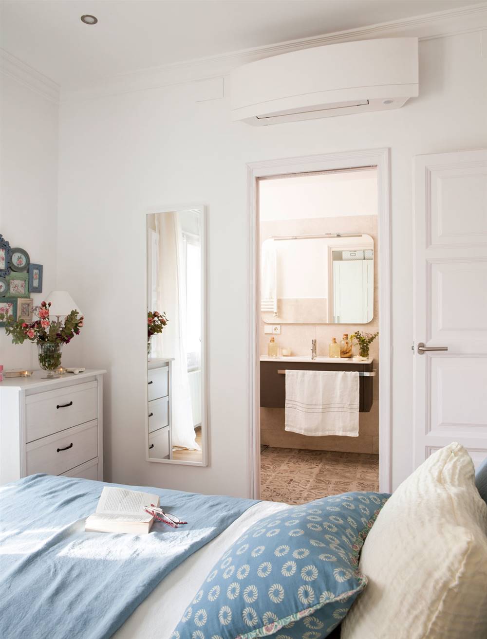 Dormitorio con comoda blanca y cojines y plaids azules y aire acondicionado 