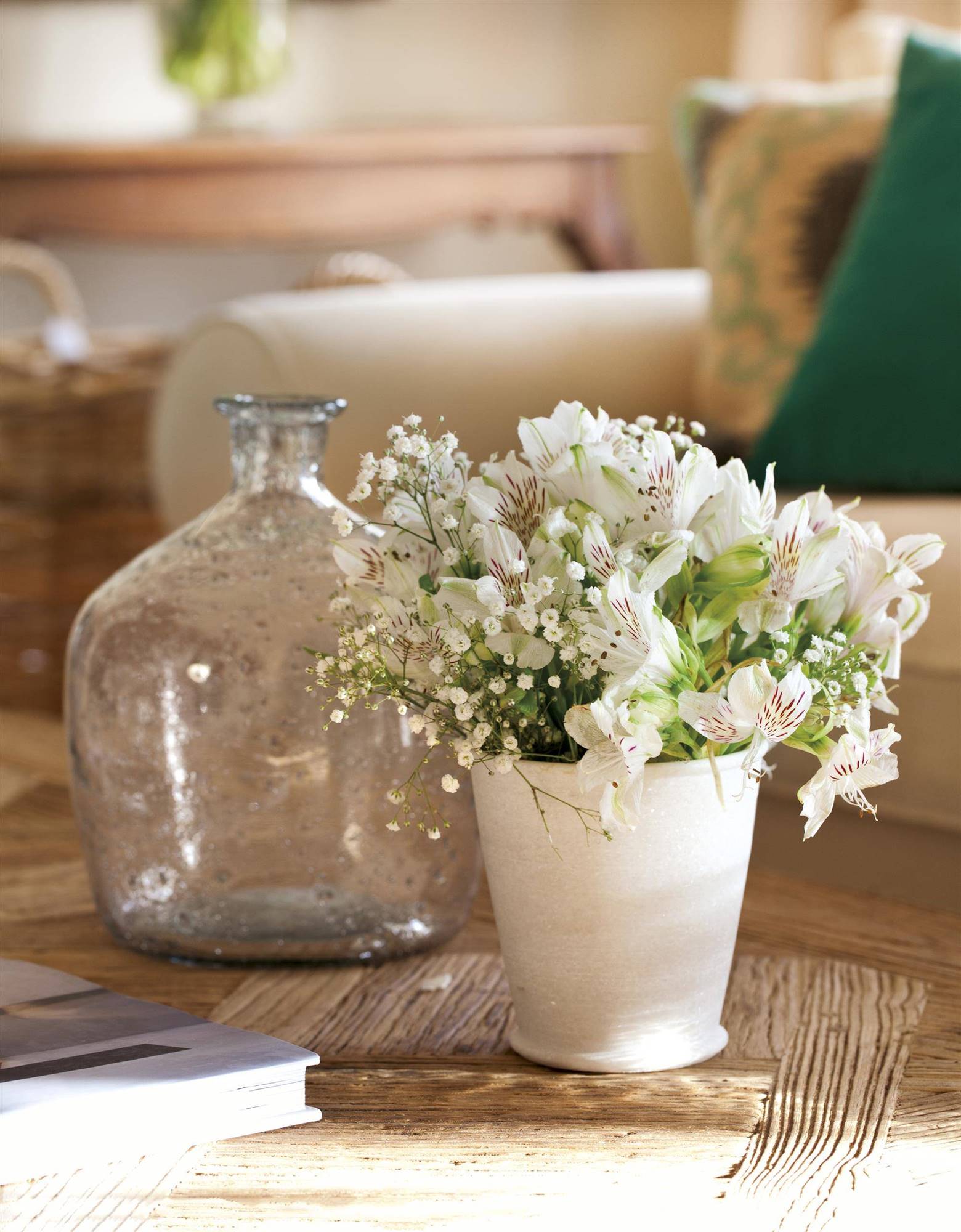Mesa de centro decorada con una damajuana y una maceta con flores blancas 00385957