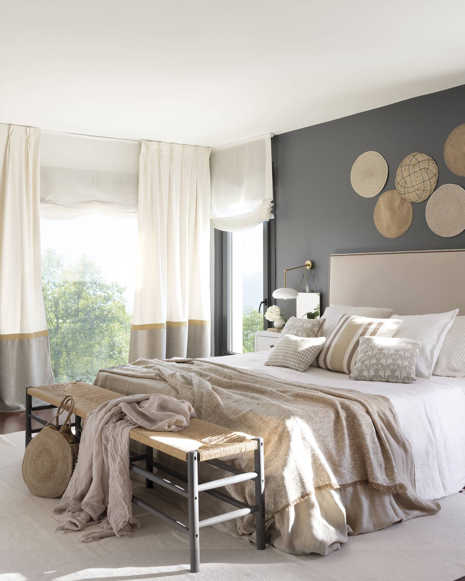 Dormitorio en tonos crudos con pared pintada de gris oscuro con banco a pié de cama de la casa de Paula Duarte.