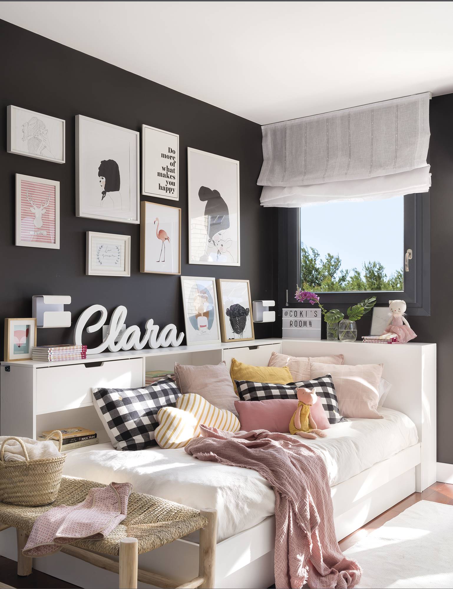 Dormitorio juvenil con pared negra, composición de cuadros y ropa de cama en blanco y rosa de la casa de Paula Duarte.