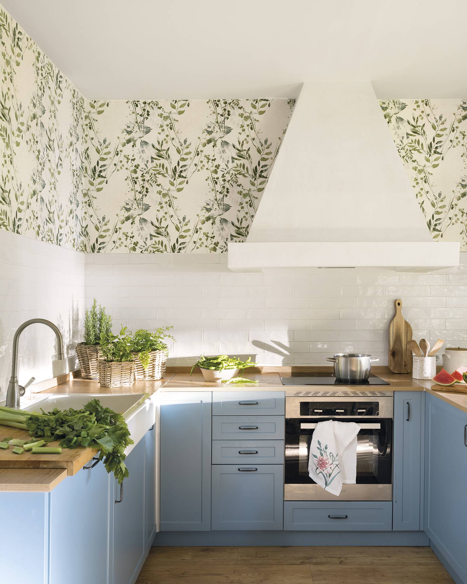 Una cocina en tonos blancos y azules con papel pintado con motivos florales en la parte superior
