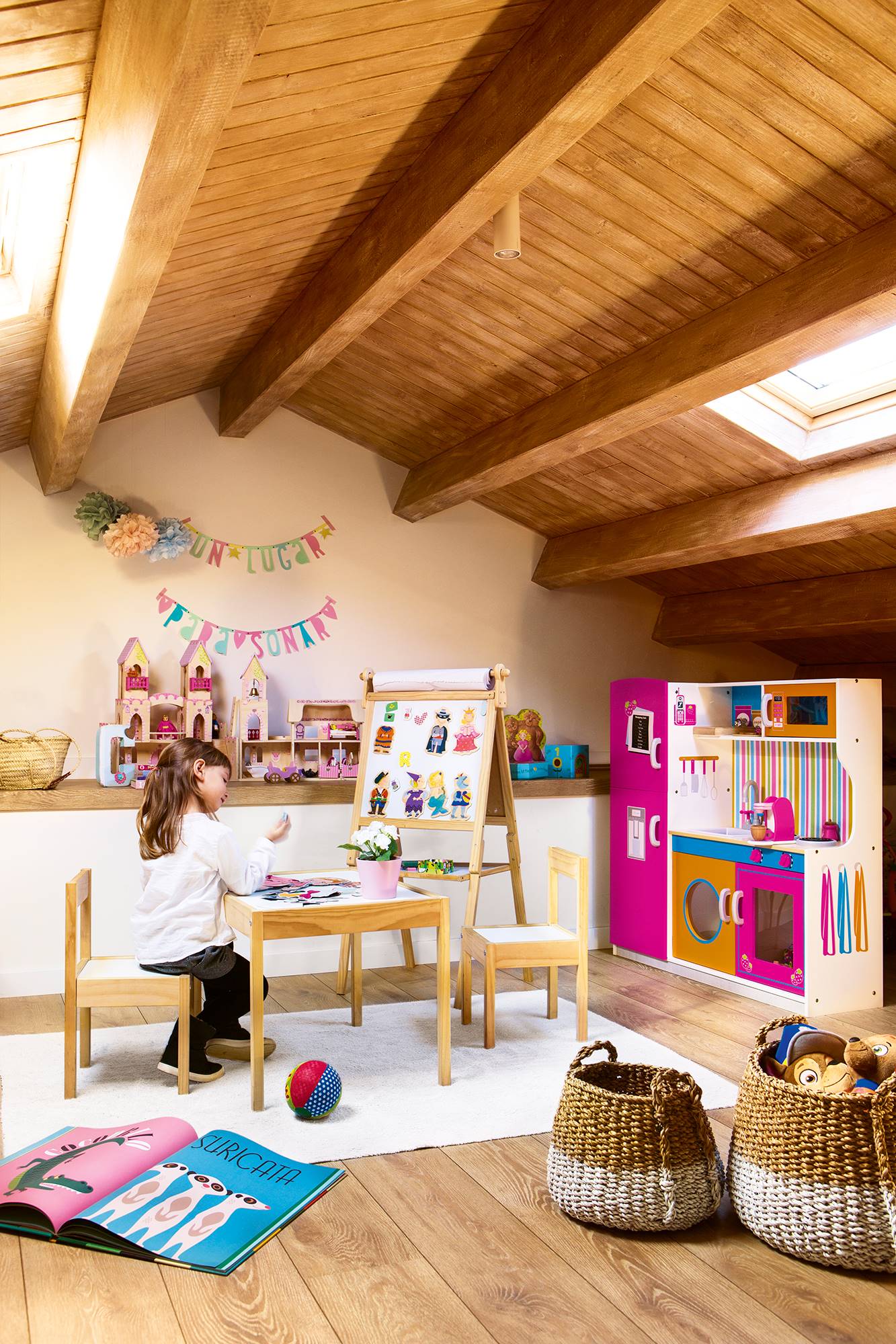 Zona de juegos infantil con mesa, dos sillas, una pizarra y una cocina de juguete