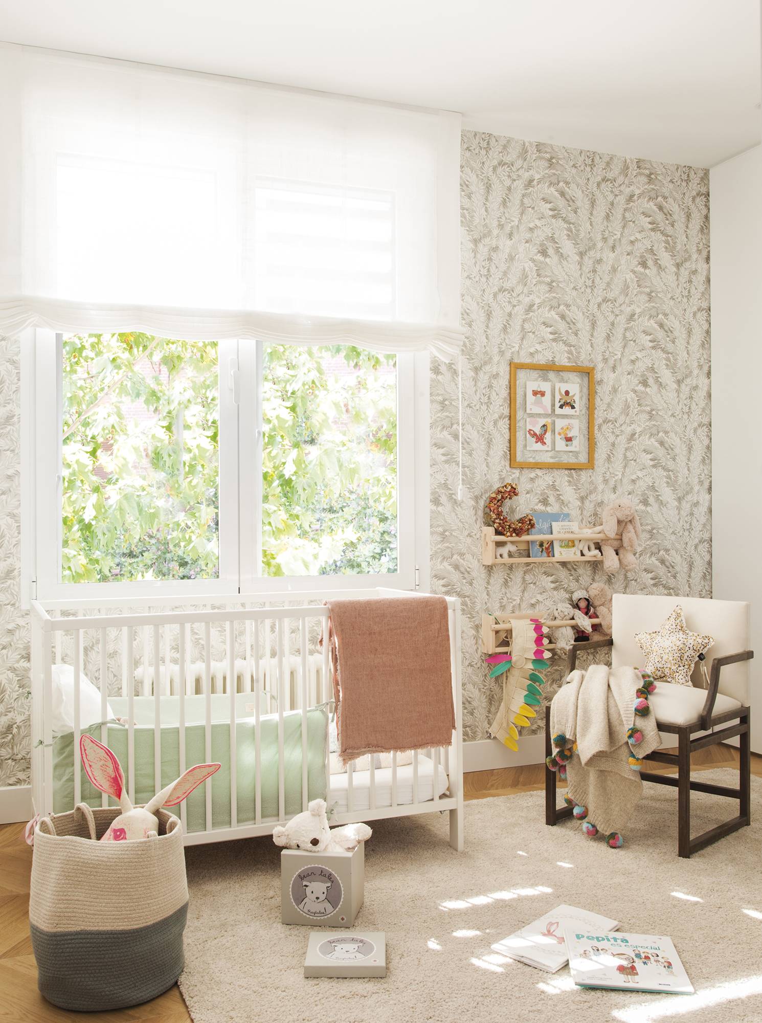 Habitación de bebé con cuna, repisas con libros, butaca y papel pintado botánico