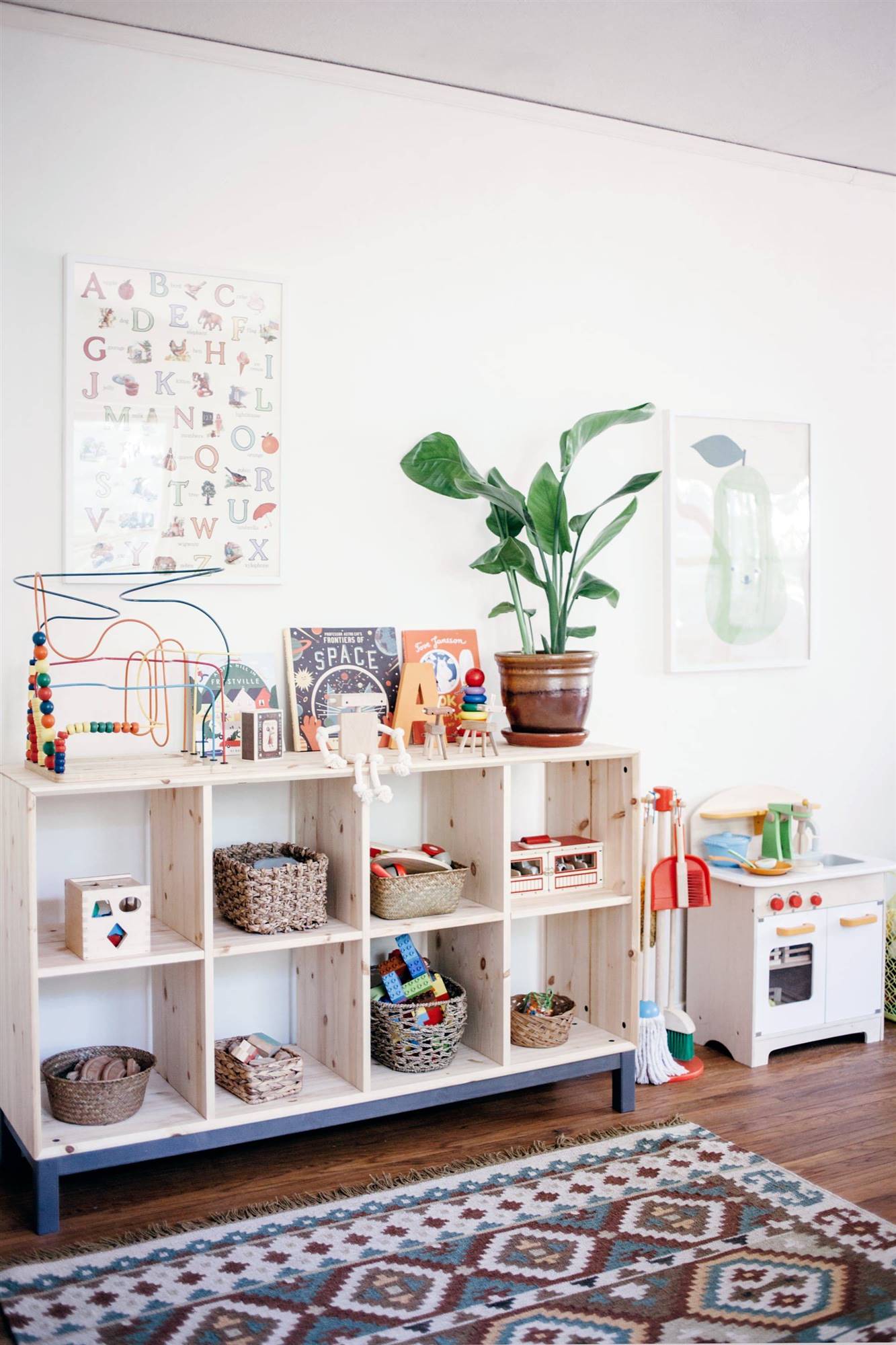 Zona de juegos infantil decorada con el método Montessori con una estantería abierta y una planta