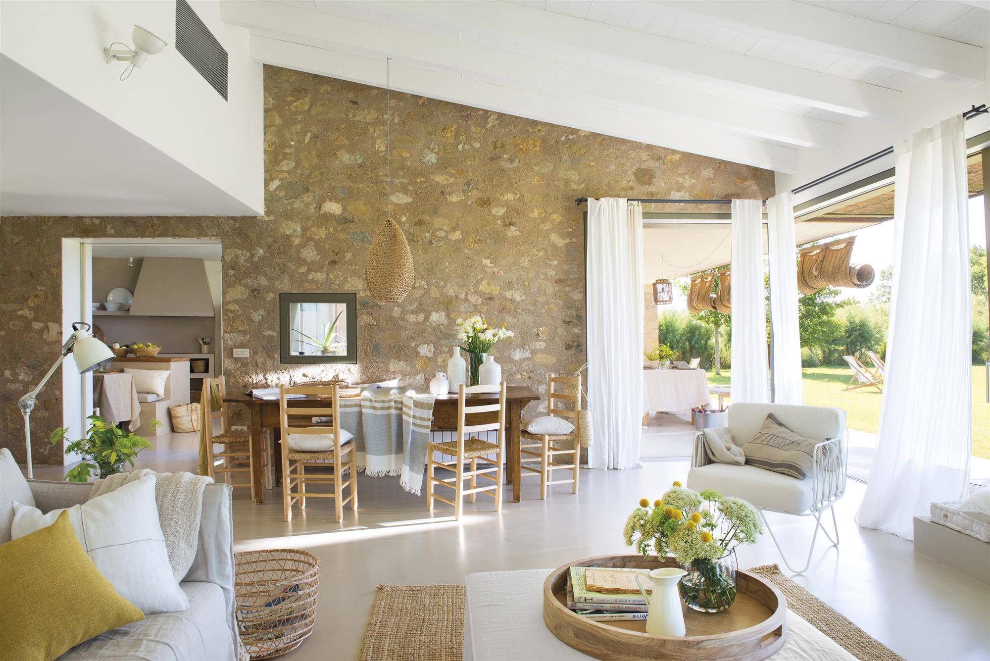 Salón comedor de casa rústica con pared de piedra y suelo de microcemento