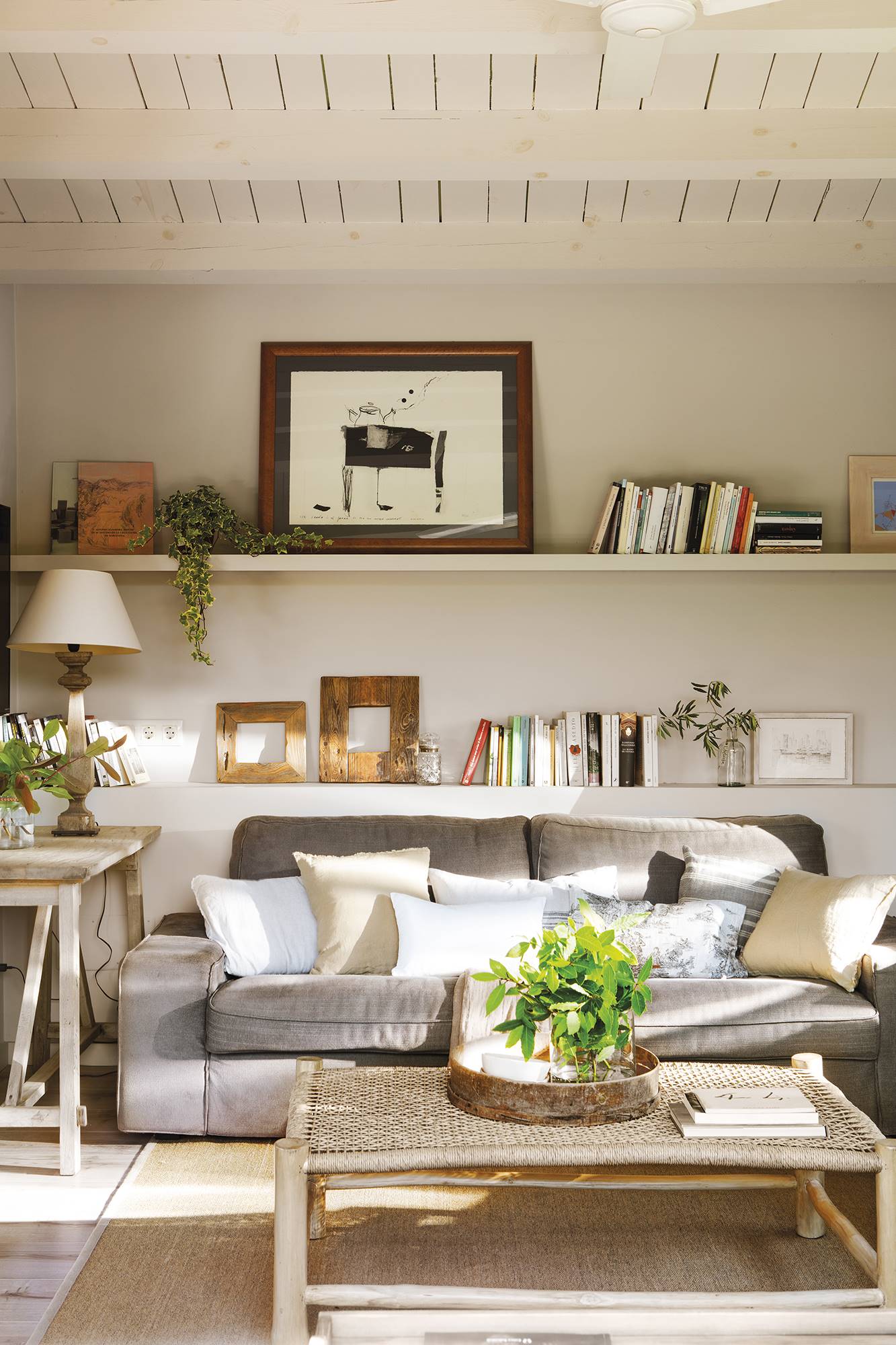 Salón con estantes con libros, sofá gris y cojines. 