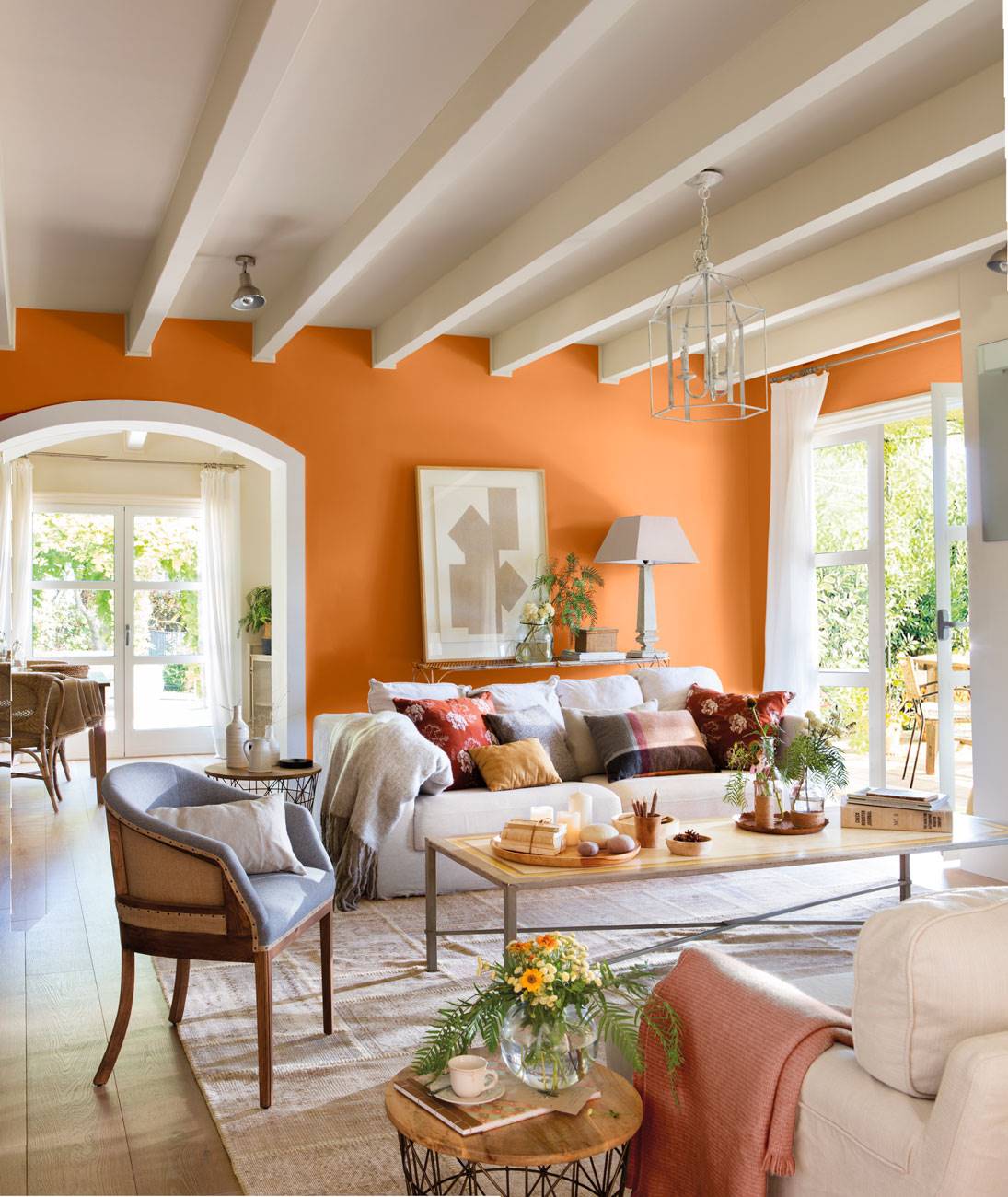Salón con vigas vistas pintadas blancas y pared naranja con sofás contrapuestos y mesa de centro sobre alfombra 438066