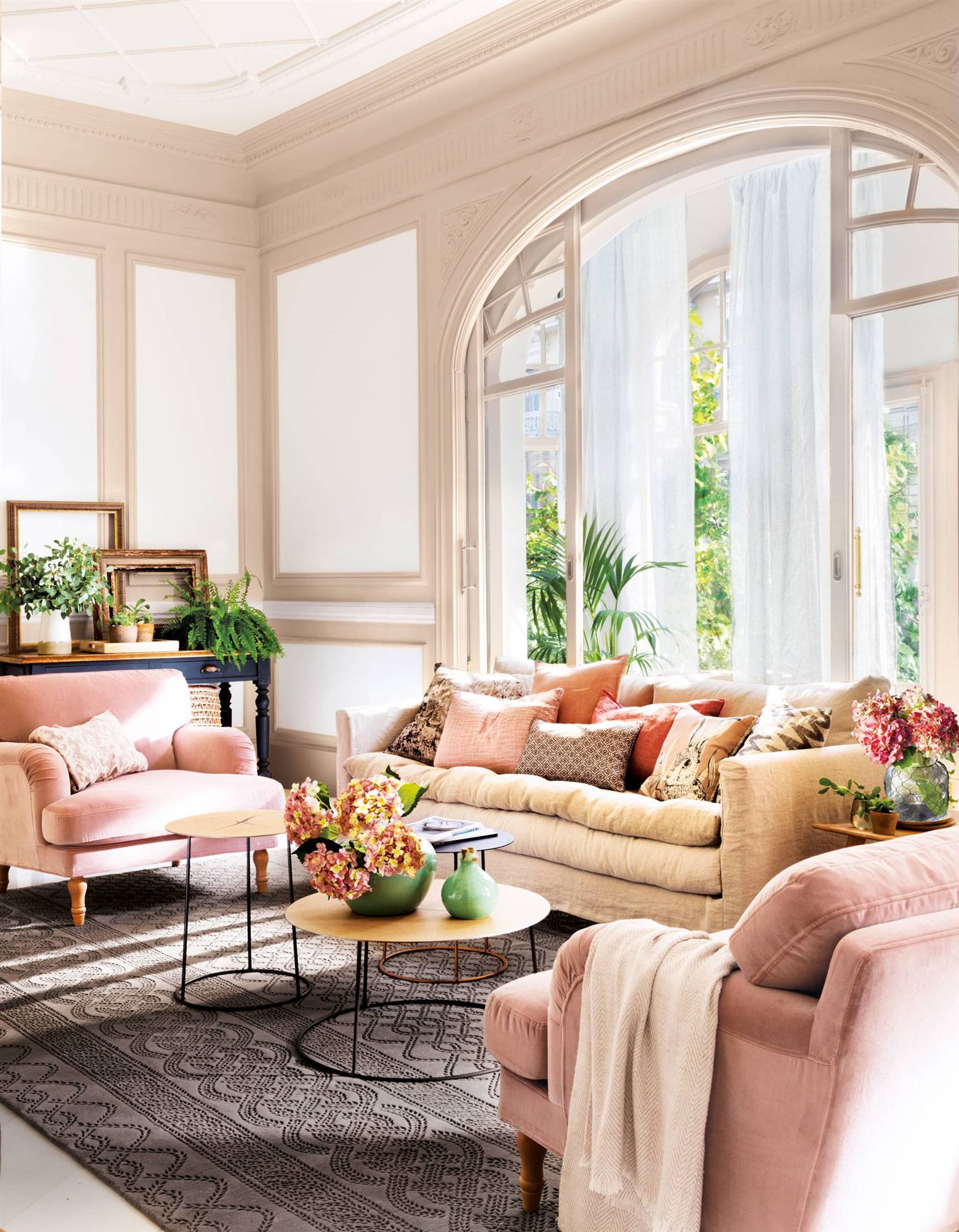 Salón señorial con ventanal en semi arco, sofá beige y butacas rosas.