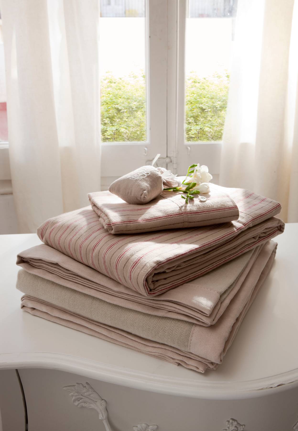 Detalle de sábanas y ropa de cama en tonos rosa y gris sobre consola_312810