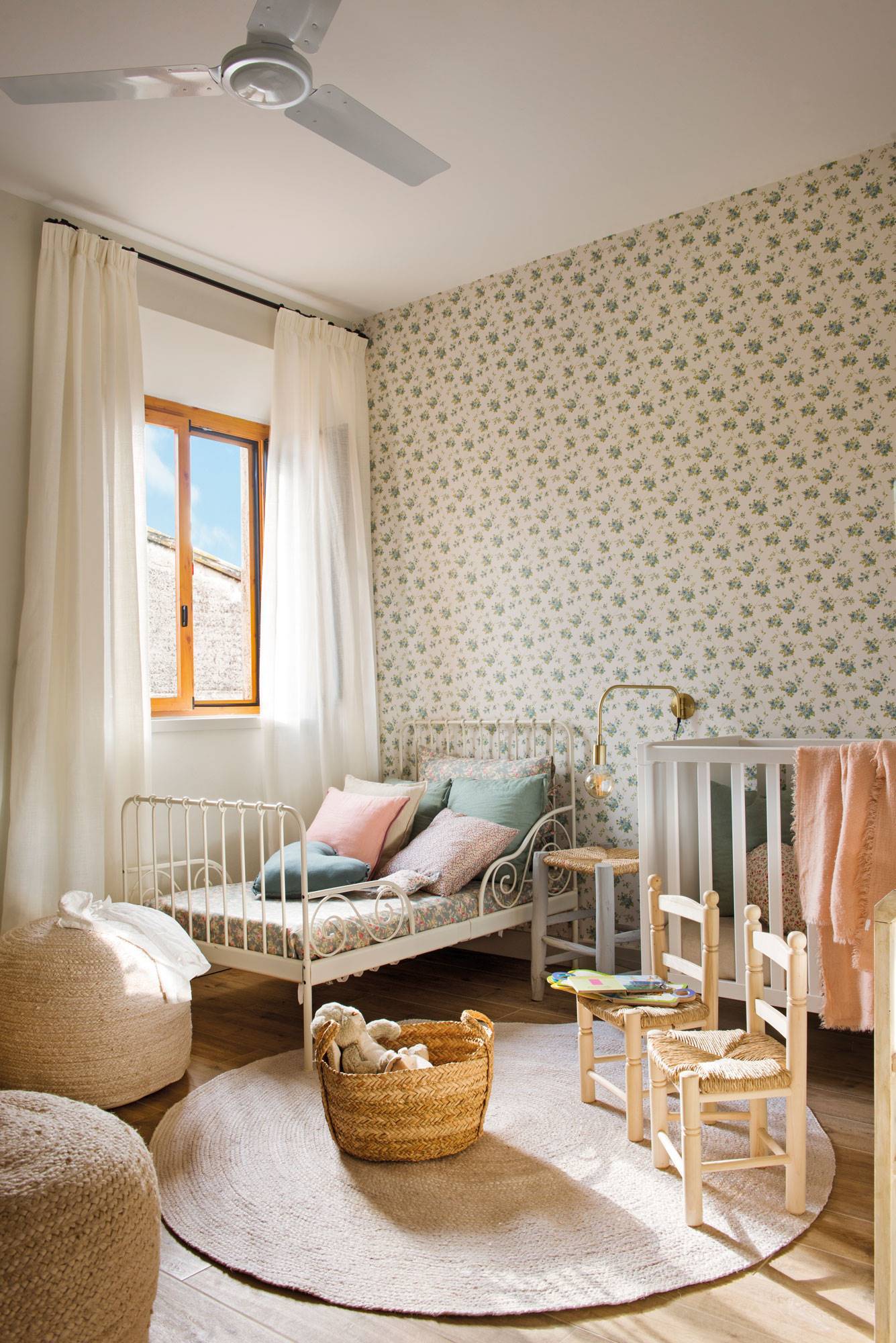 Habitación infantil con papel pintado, alfombra y puffs de fibras y cuna.
