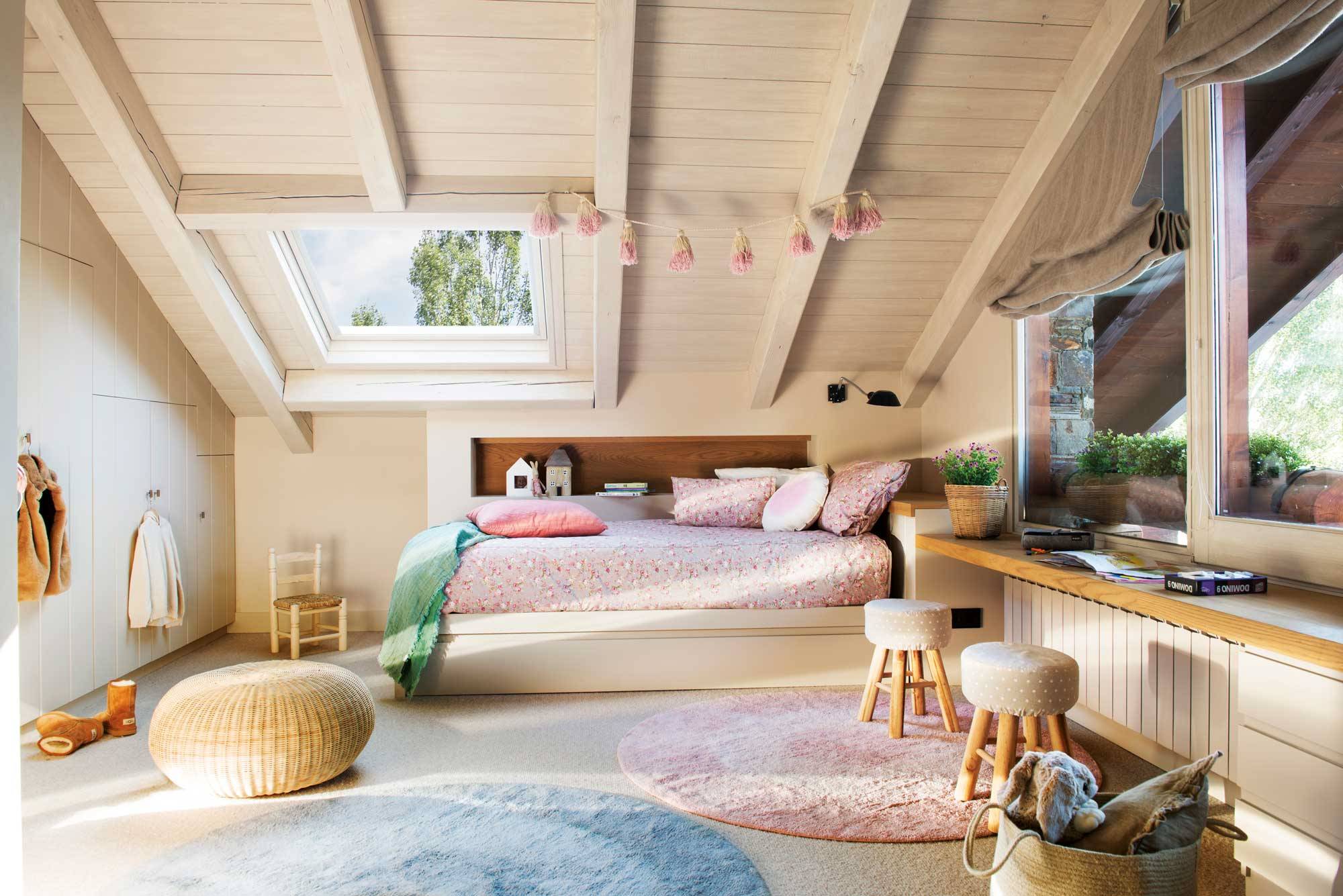 Dormitorio infantil en buhardilla con cama rosa, puff y taburetes.