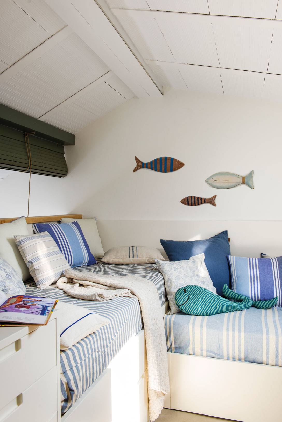 Dormitorio marinero en blanco y azul con dos camas y peces decorativos en la pared.