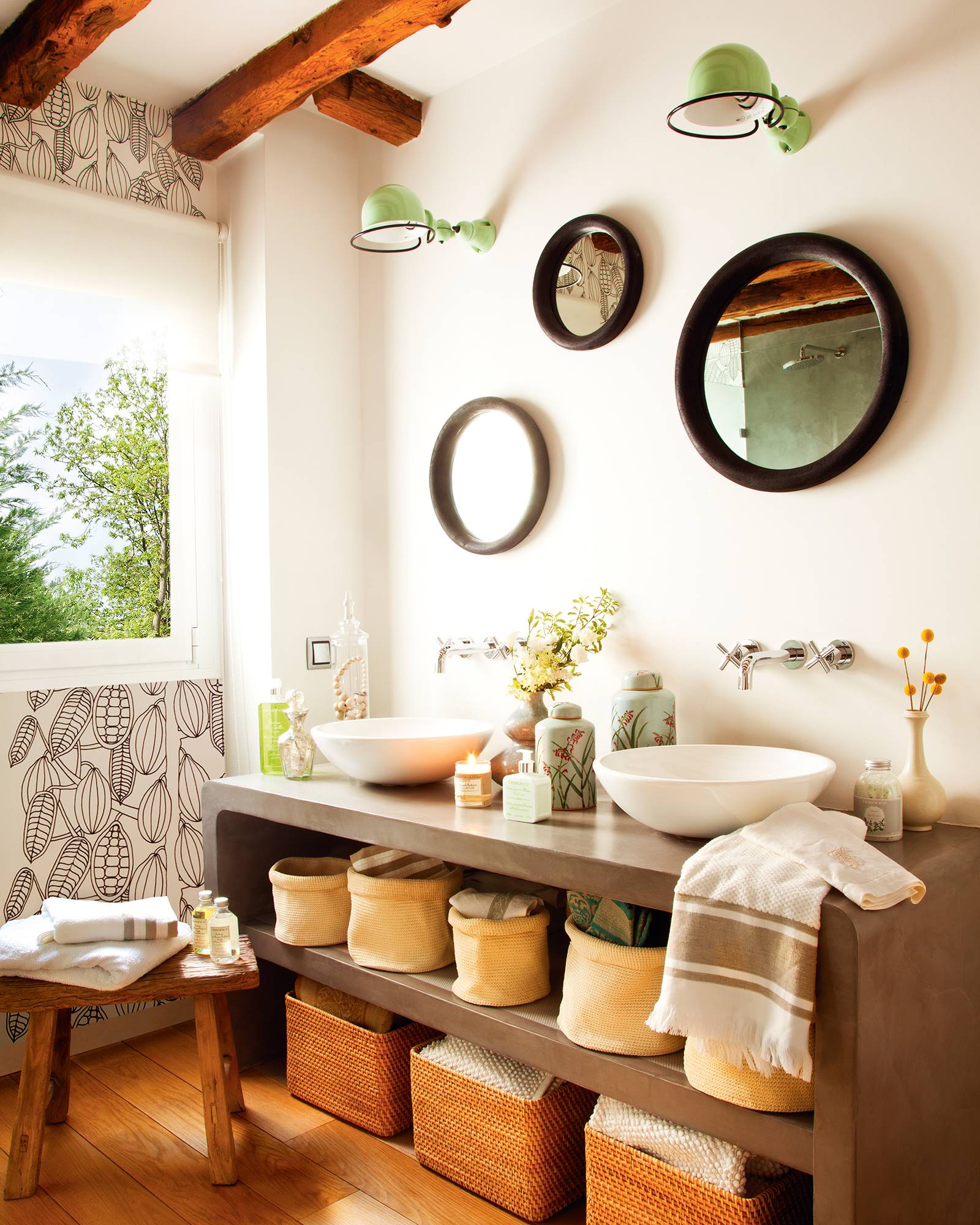 Baño con pared empapelada y tres espejos redondos de diferente tamaño.