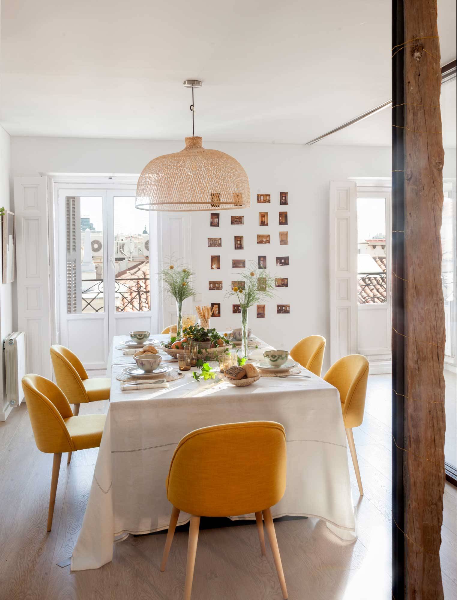 Comedor con mesa, sillas tapizadas en amarillo y pared blanca decorada con fotos tipo Polaroid.