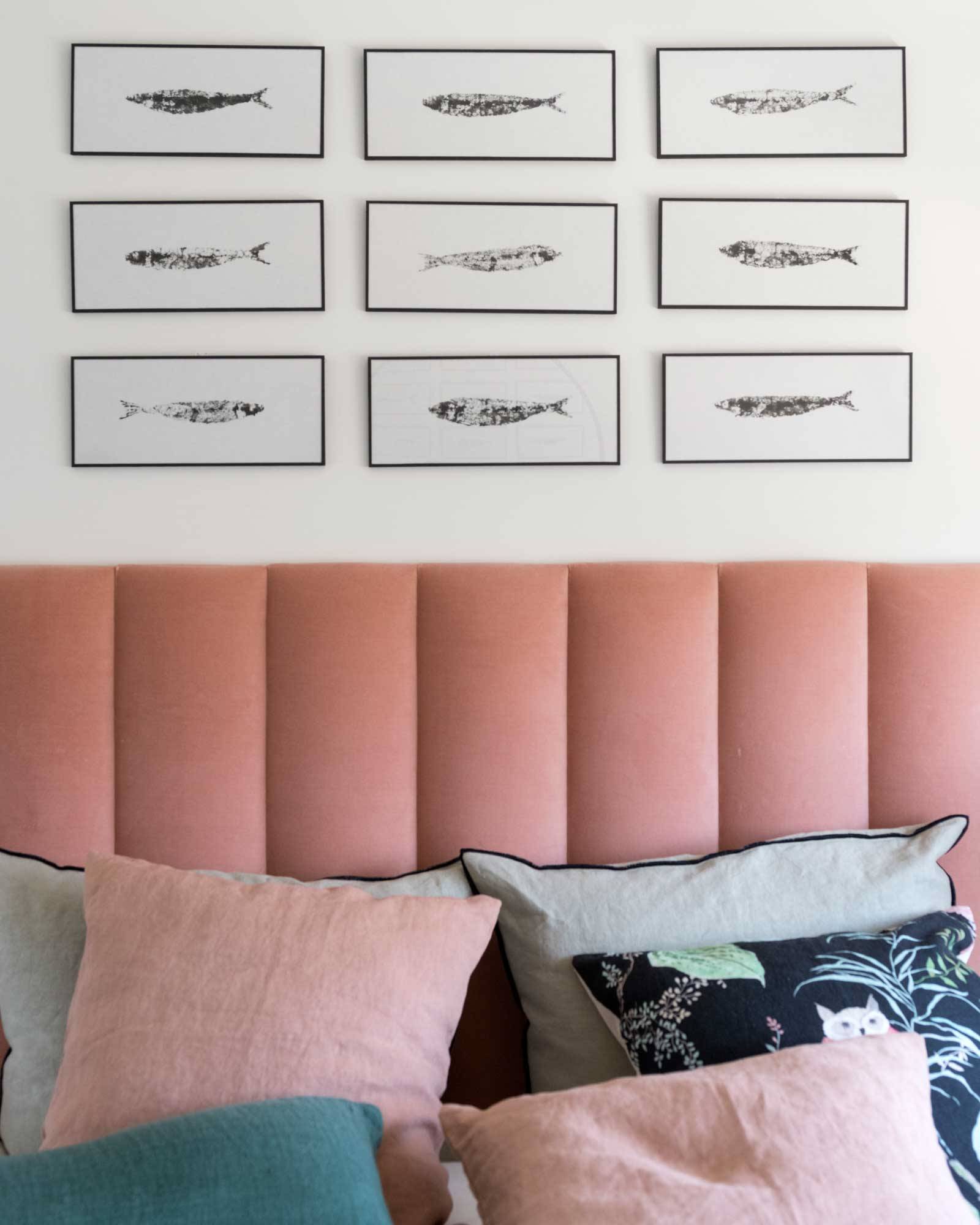 Dormitorio con pared del cabecero rosa decorada con una composición de cuadros.