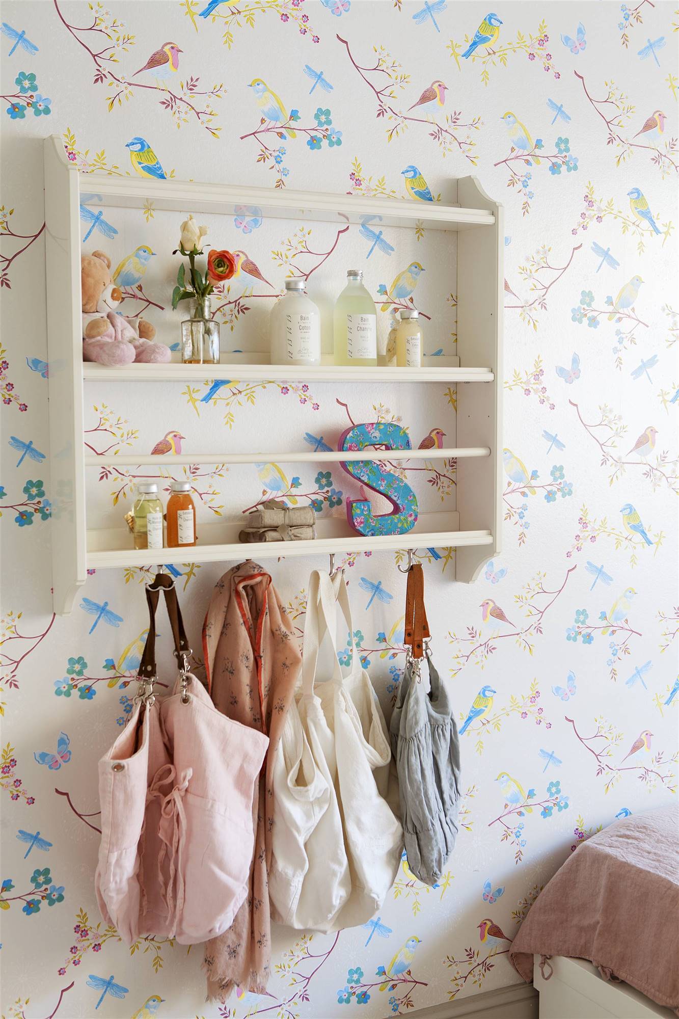 Habitación infantil con papel pintado de pájaros en la pared y perchero blanco.