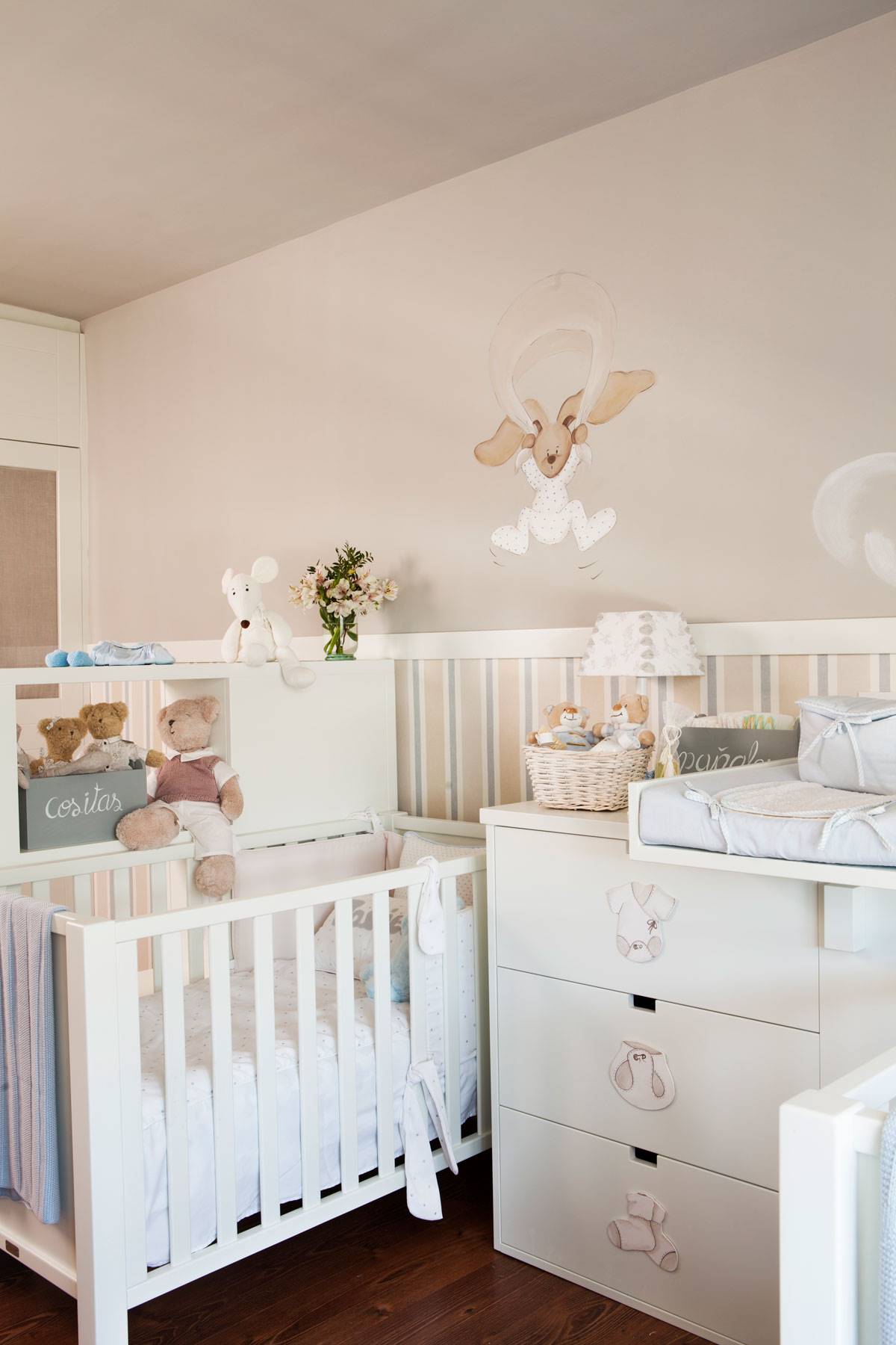 Habitación de bebé con arrimadero, cuna, cambiador y dibujos decorativos en la pared.
