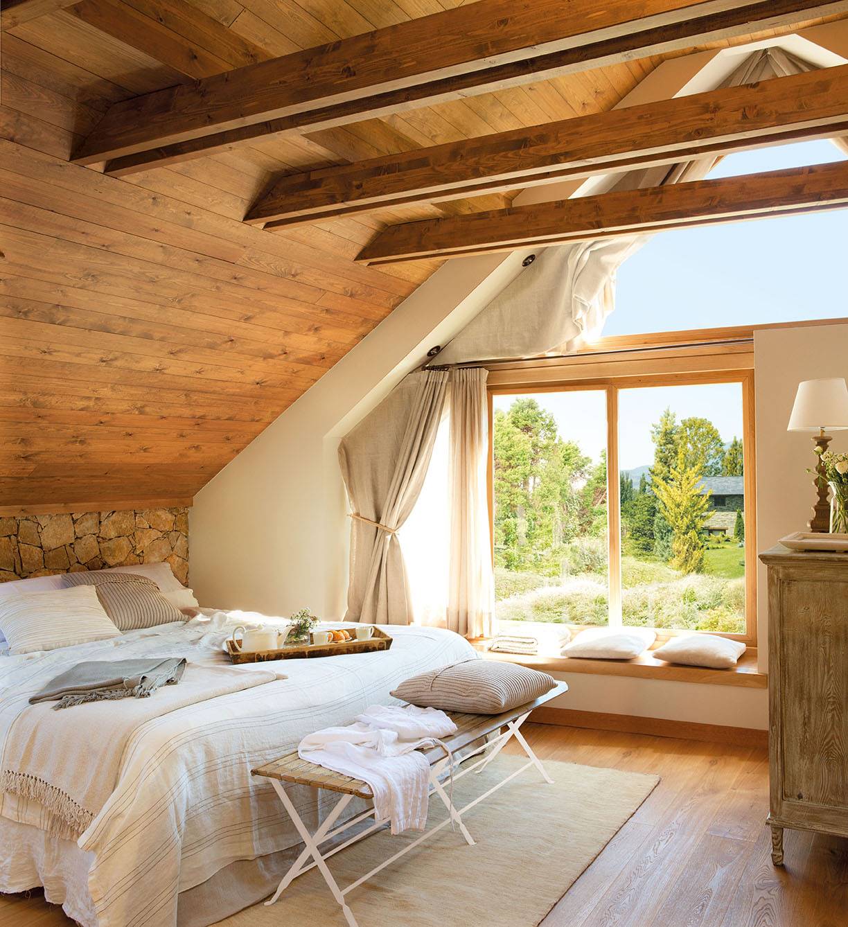 Dormitorio de casa de montaña abuhardillado y revestido de madera con ventana panorámica.