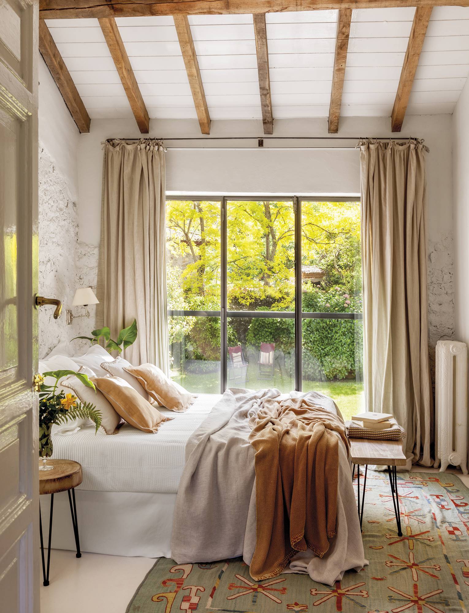 Dormitorio con vigas de madera y gran ventanal al jardín. 