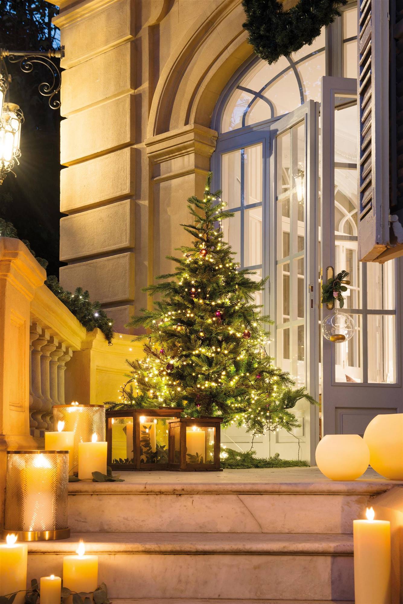 Árbol de Navidad iluminado en la entrada con velas en la escalera. 