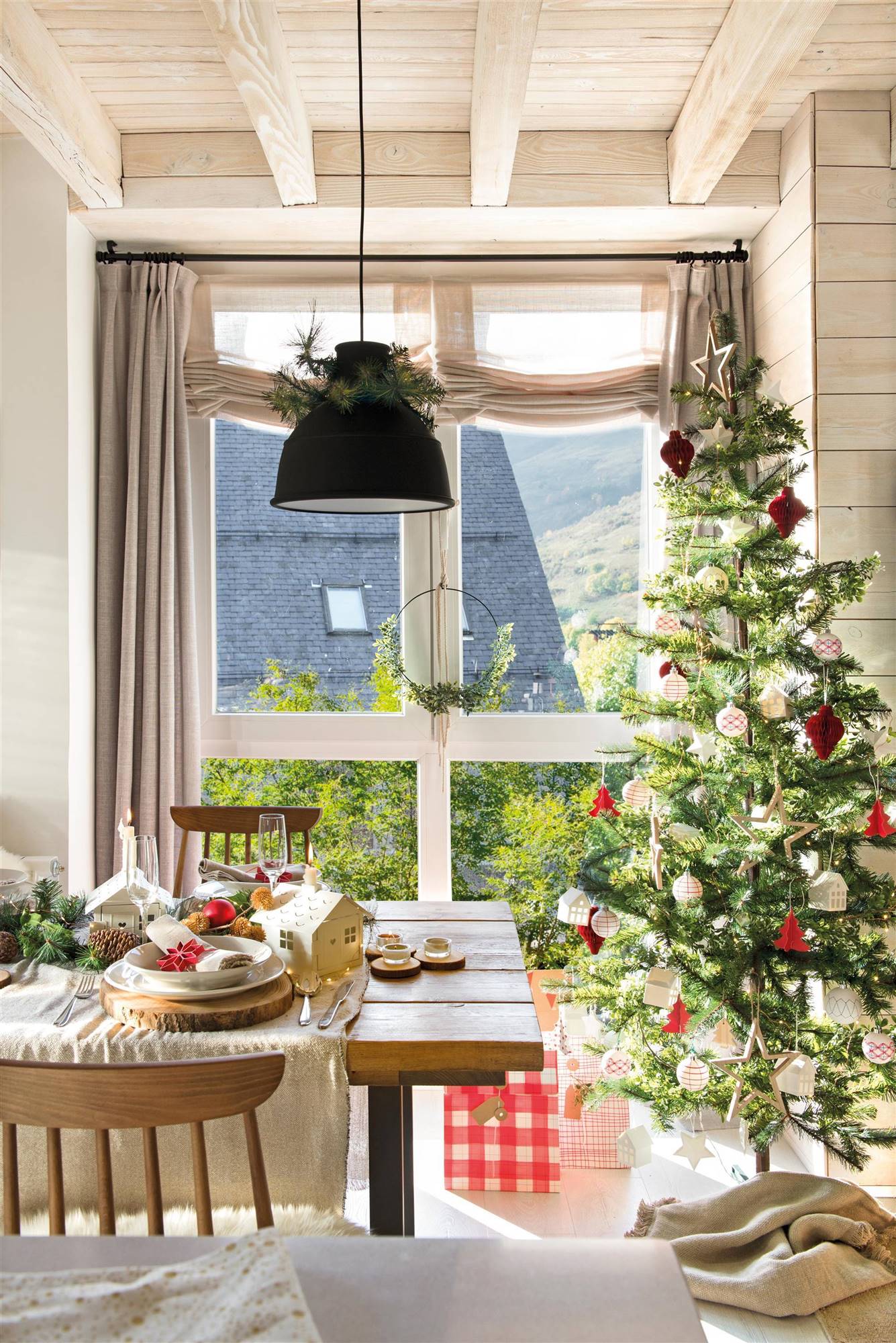 Comedor rústico con árbol de Navidad decorado en blanco y rojo junto a la mesa.