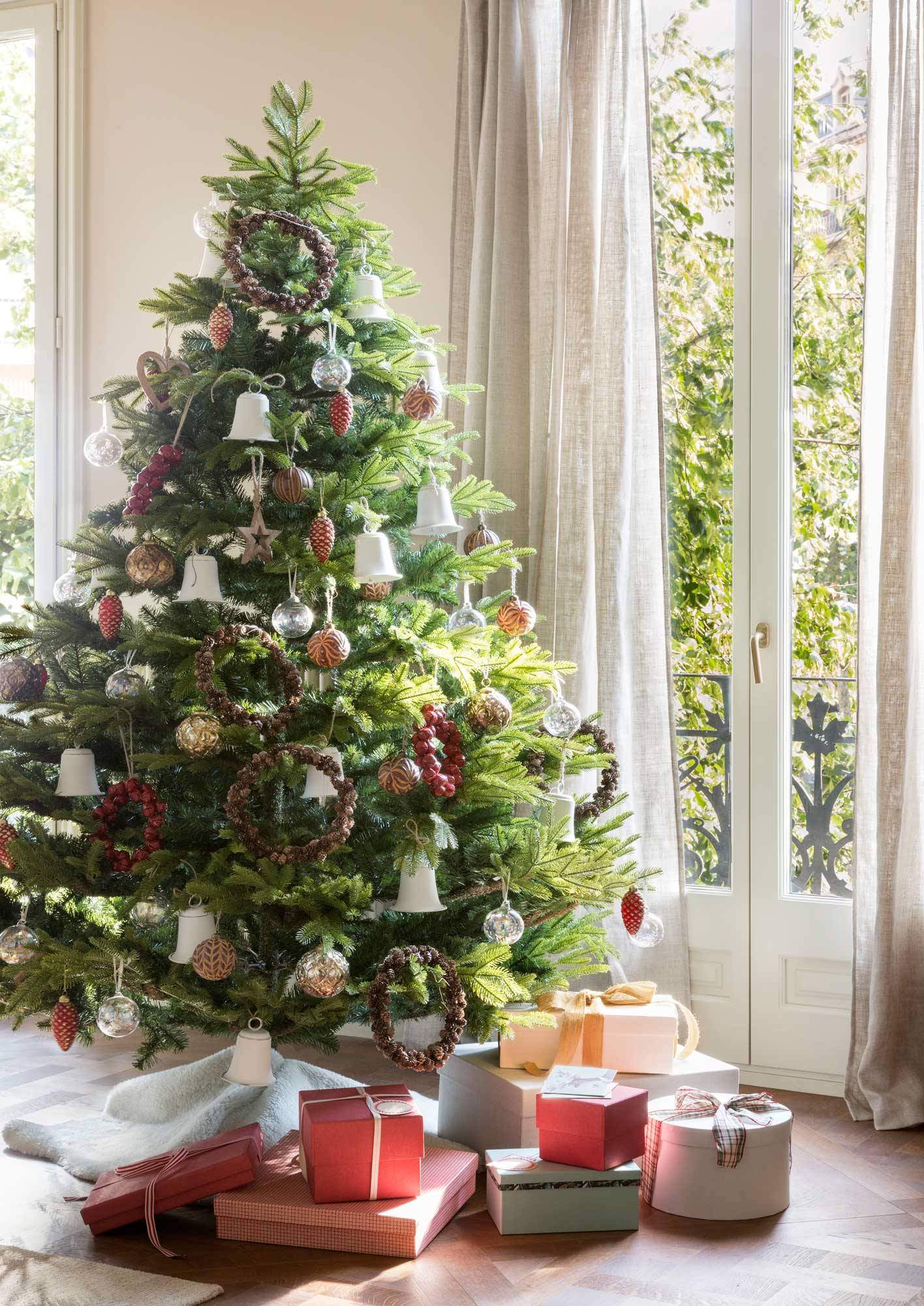 Salón con árbol de Navidad junto a la ventana con regalos debajo. 