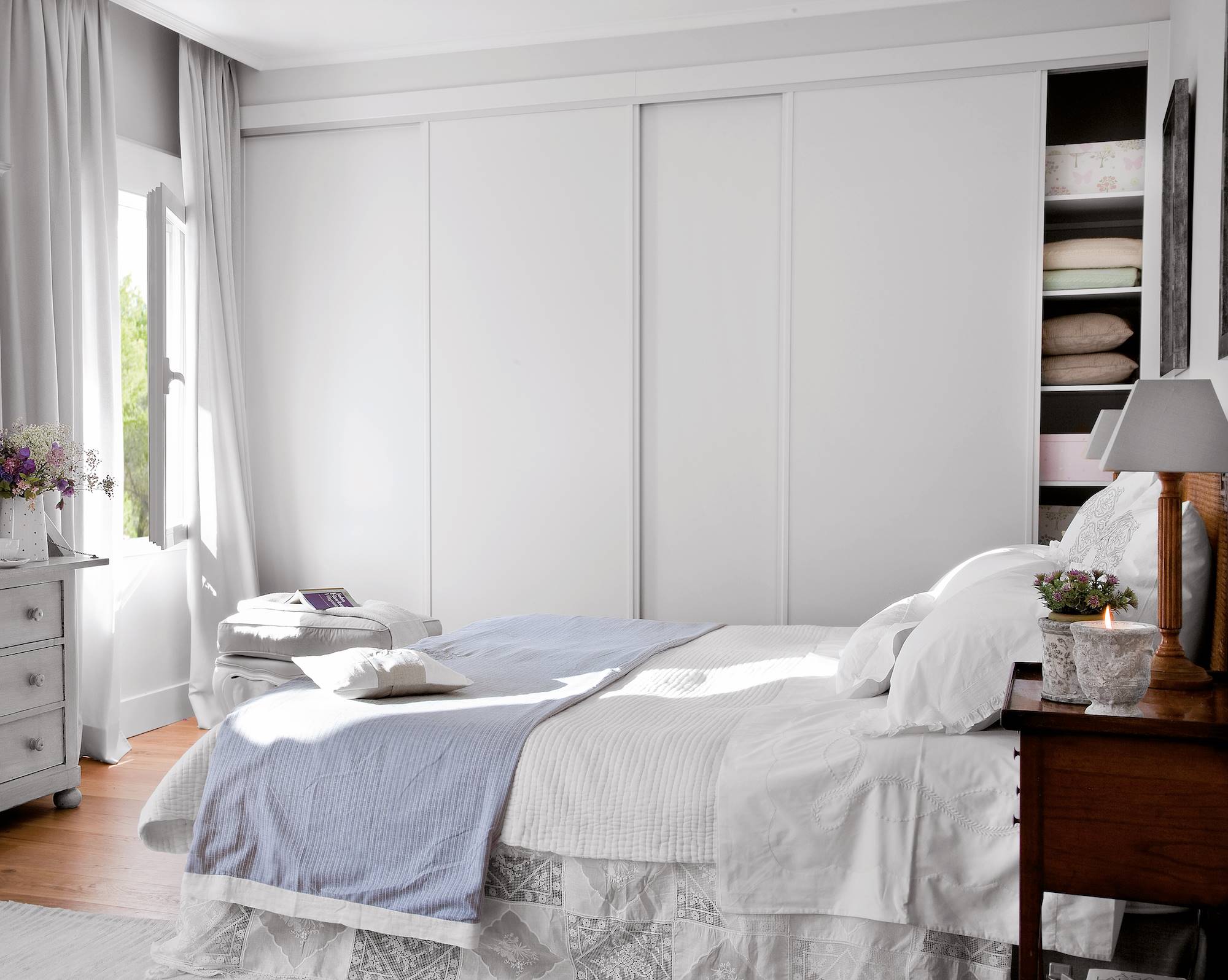 DOrmitorio con cama, ropa de cama blanca, cortinas y armario empotrado en gris claro.