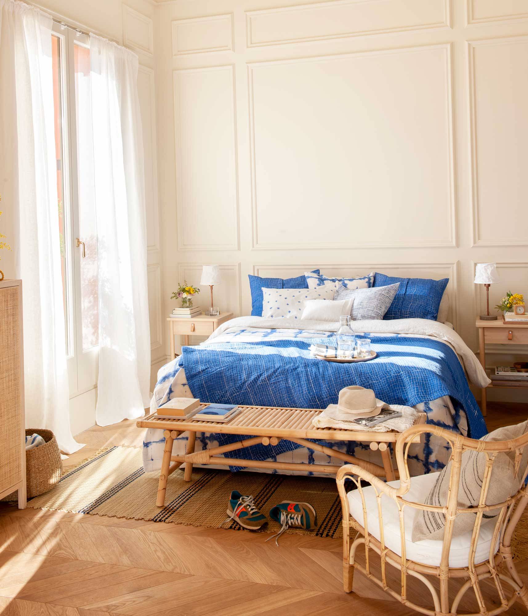 Dormitorio con molduras en la pared, muebles de madera y fibras naturales, y ropa de cama en azul. 