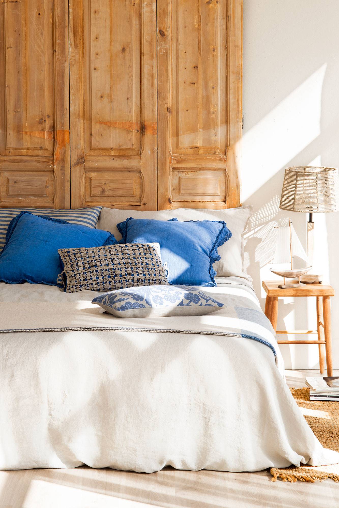 Dormitorio con cabecero hecho con puerta de madera restaurada y ropa de cama blanca y azul. 