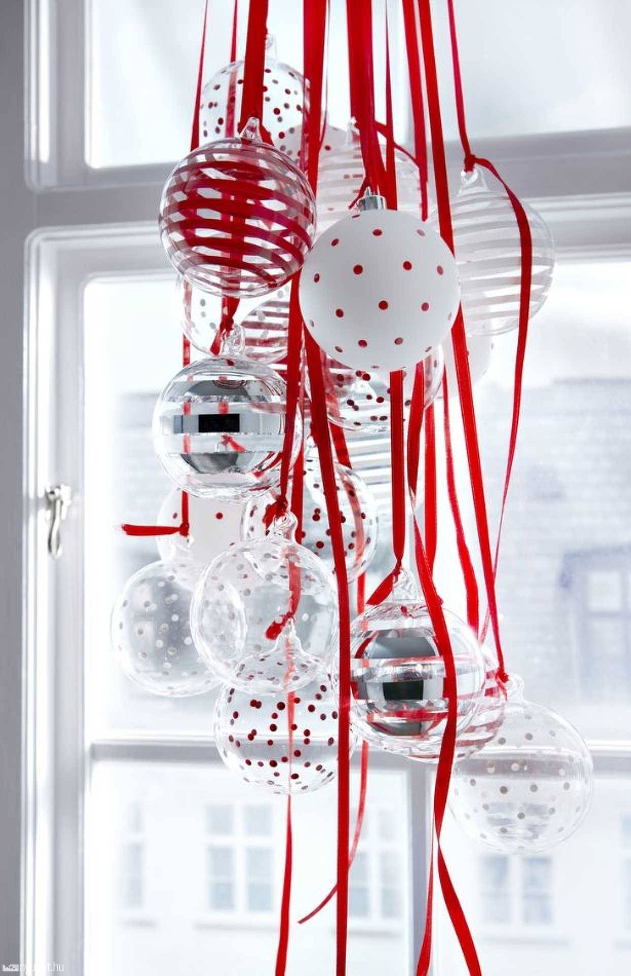 Bolas de Navidad con cintas rojas colgadas junto a la ventana.