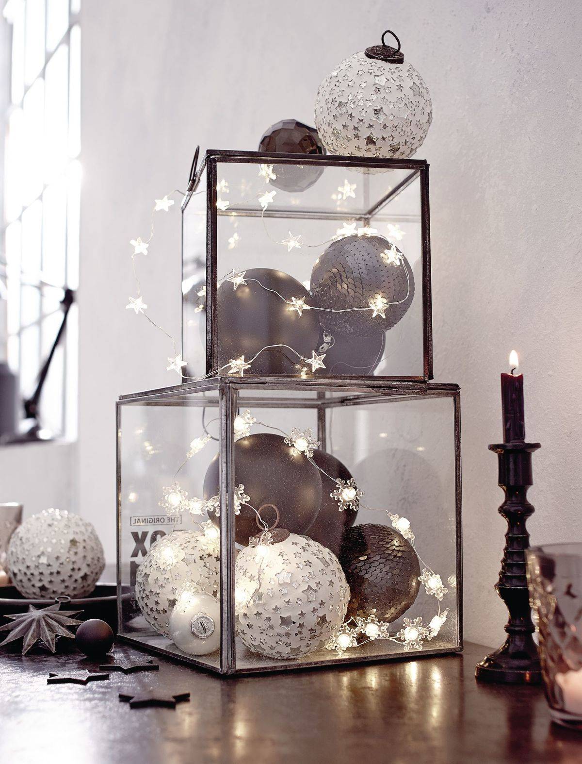 Cajas de cristal con bolas navideñas en tonos grises y guirnaldas de luces
