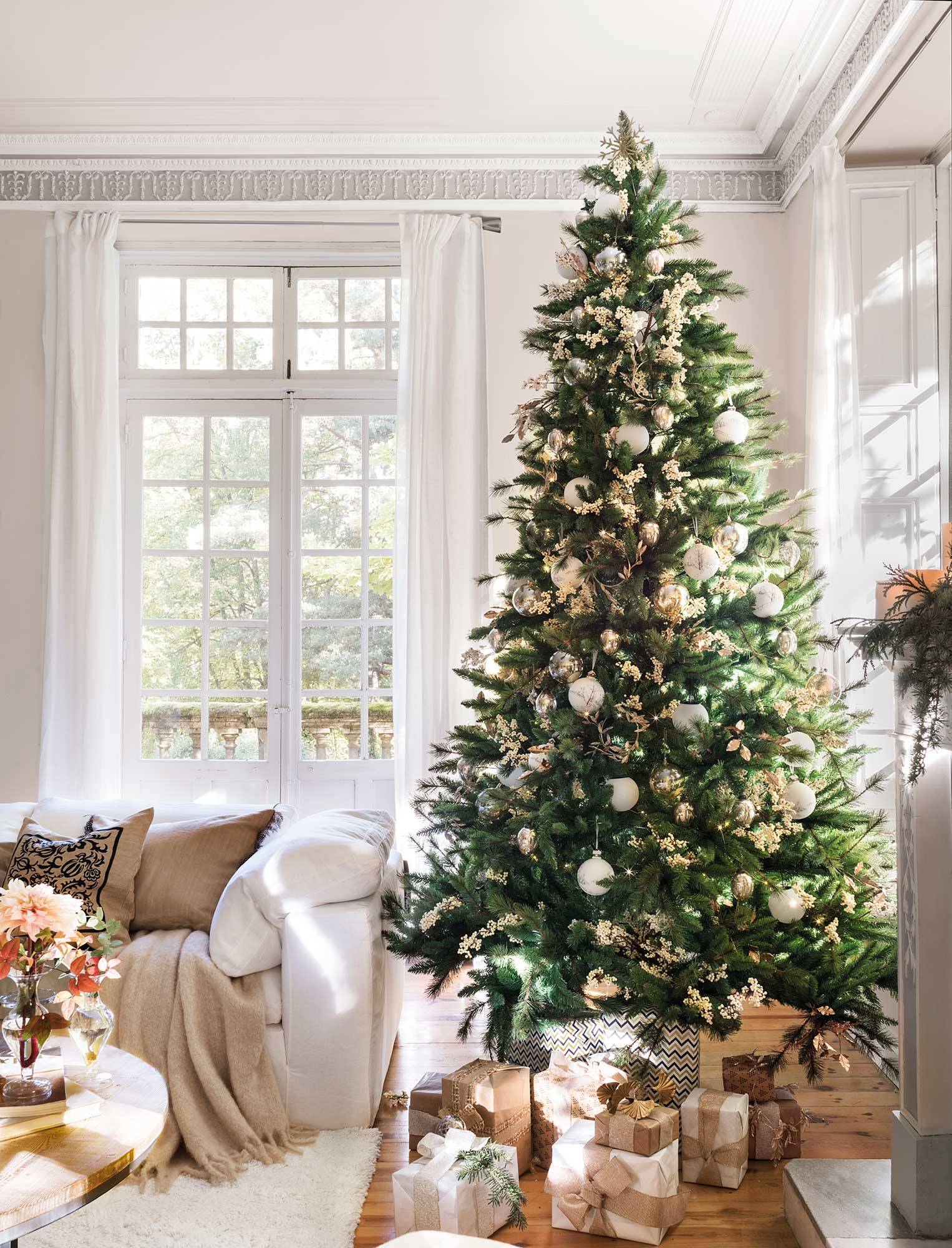Salón con árbol de Navidad grande y adornos blancos.
