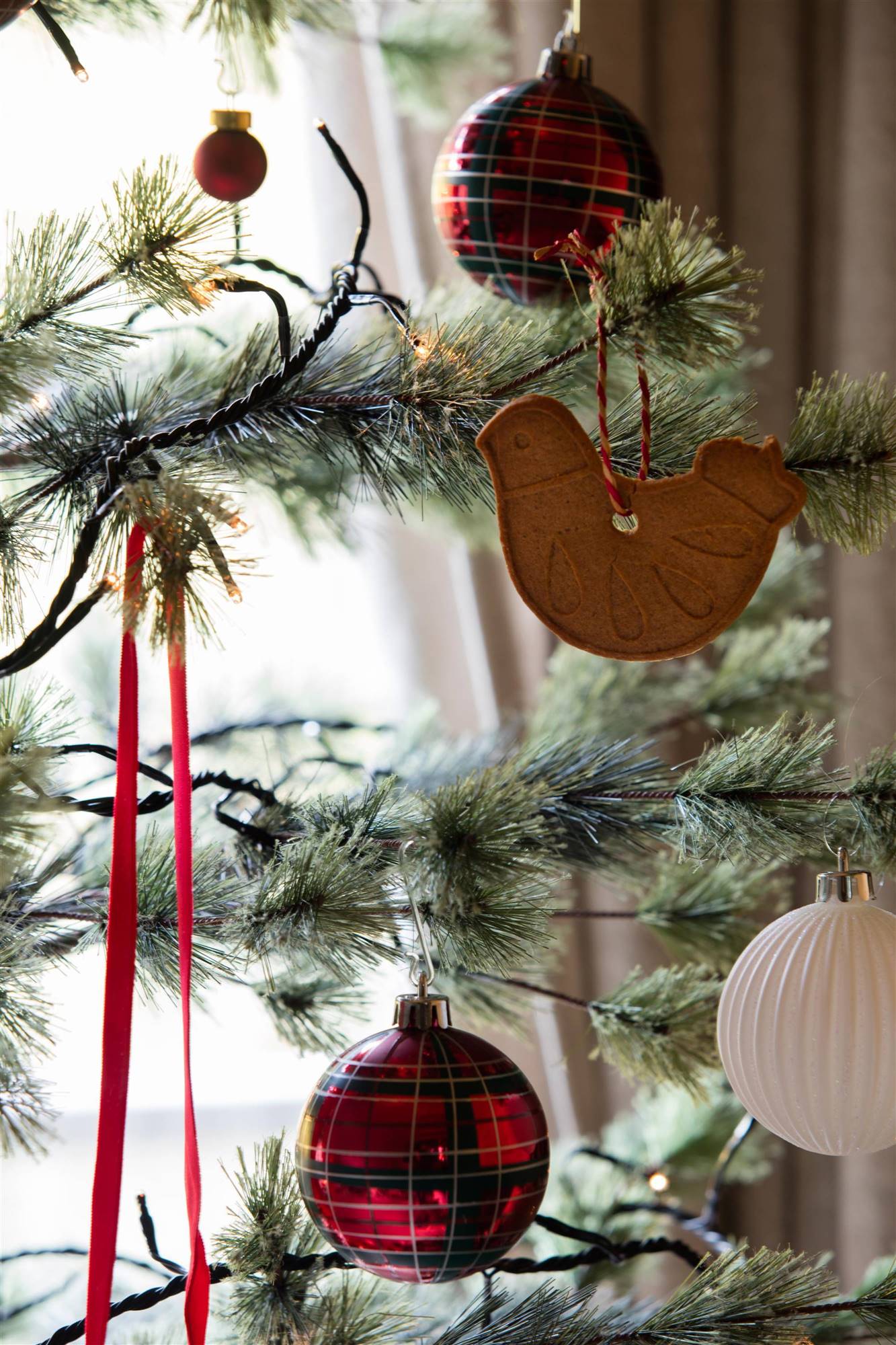 Árbol de Navidad con bola de cuadros, galleta en forma de pájaro y cintas de raso en color rojo.