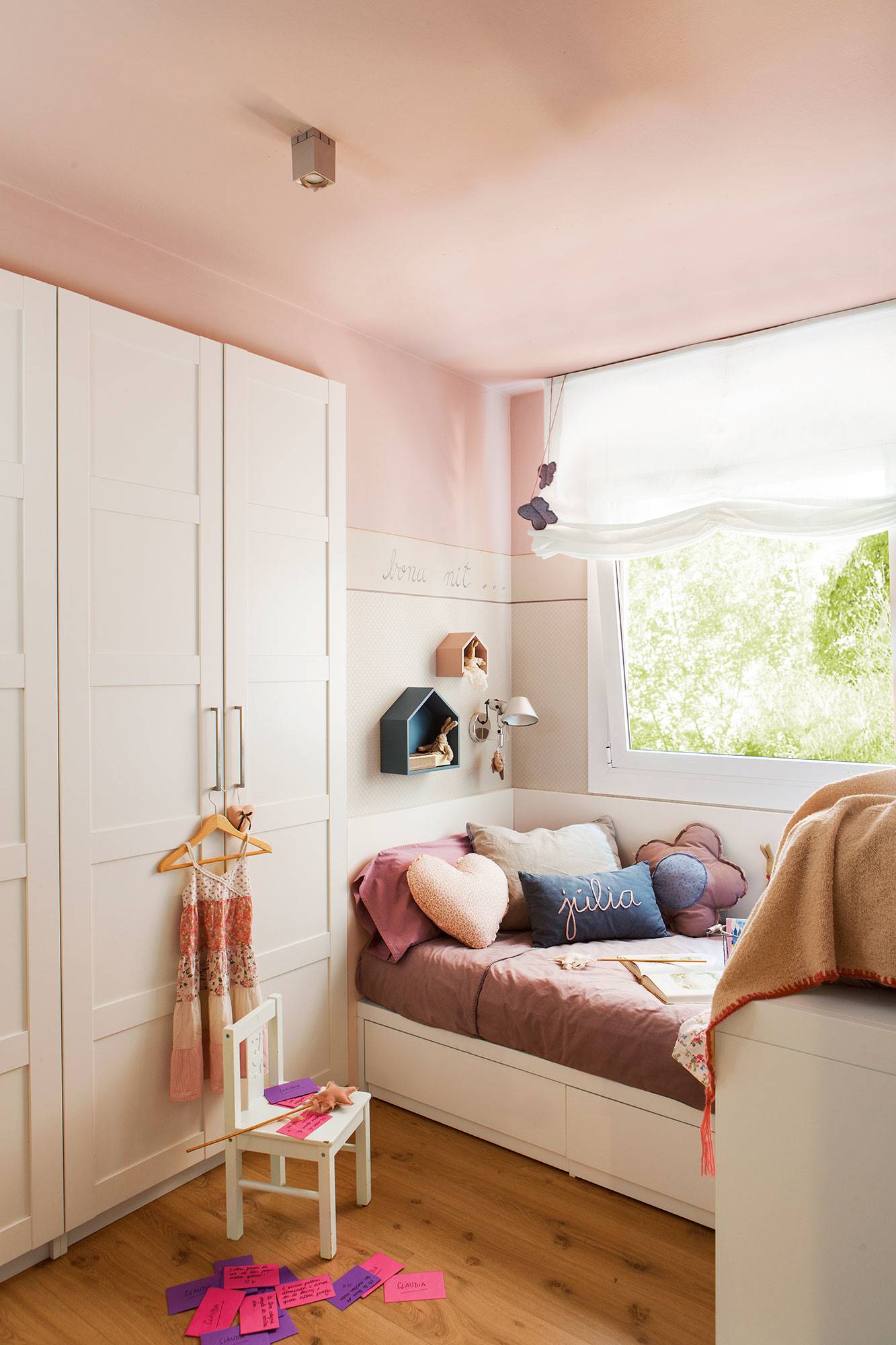 Dormitorio infantil en rosa con cama arrimada a la pared bajo la ventana y armario empotrado en blanco