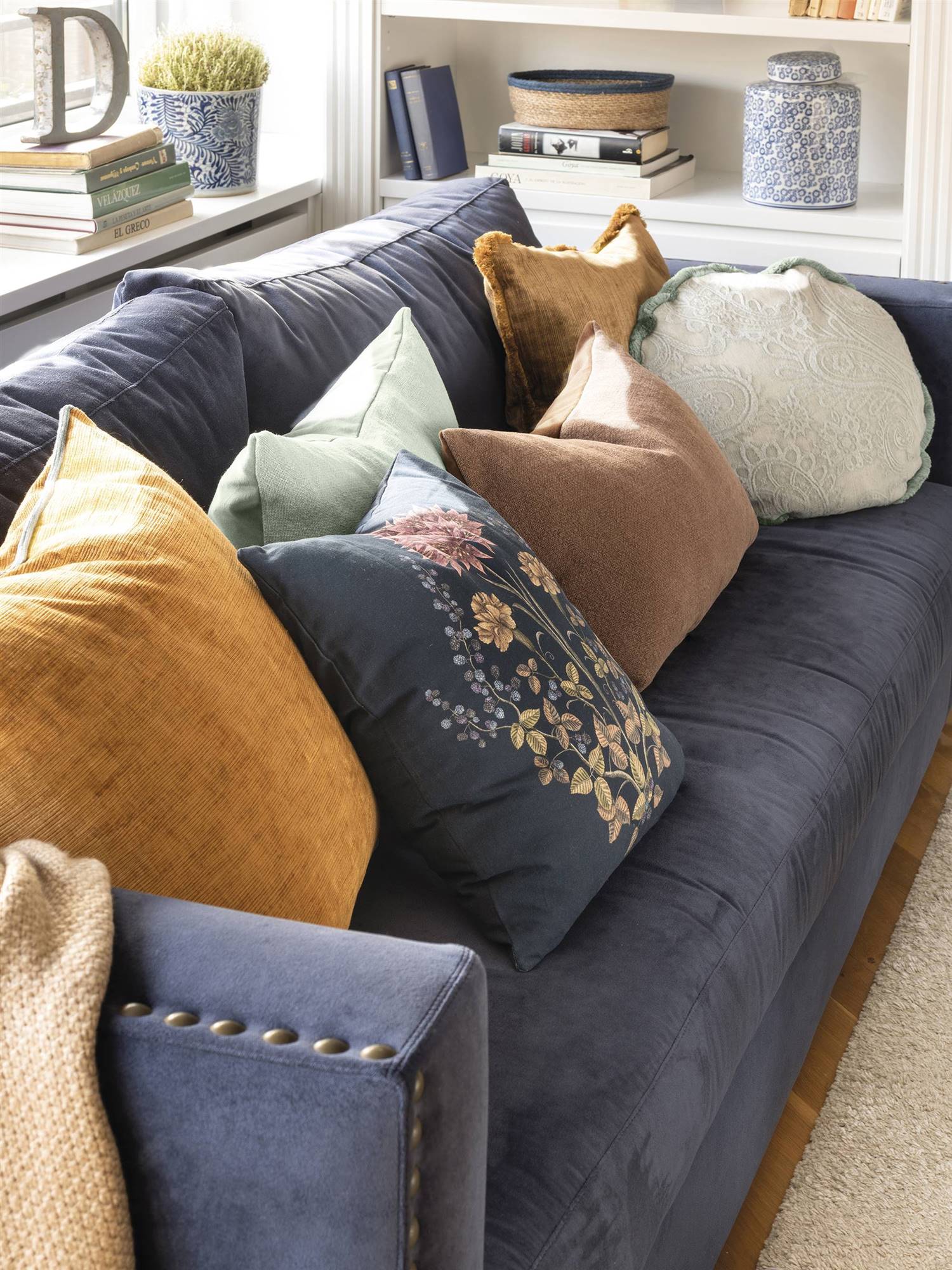 Salón con sofá azul con tachuelas y cojines de varios colores. 