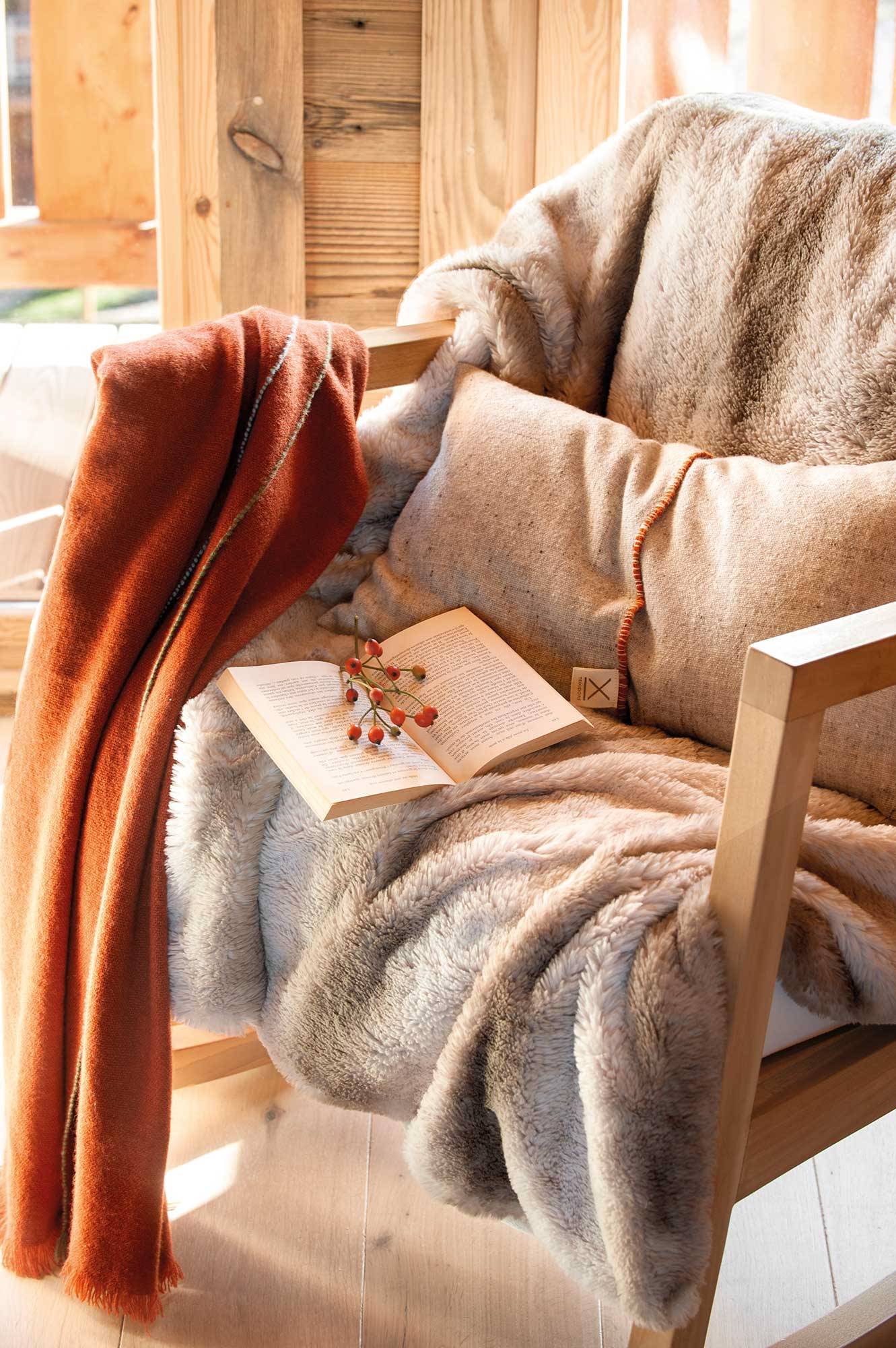 Salón rústico con butaca de madera con mantas, cojines y plaids. 