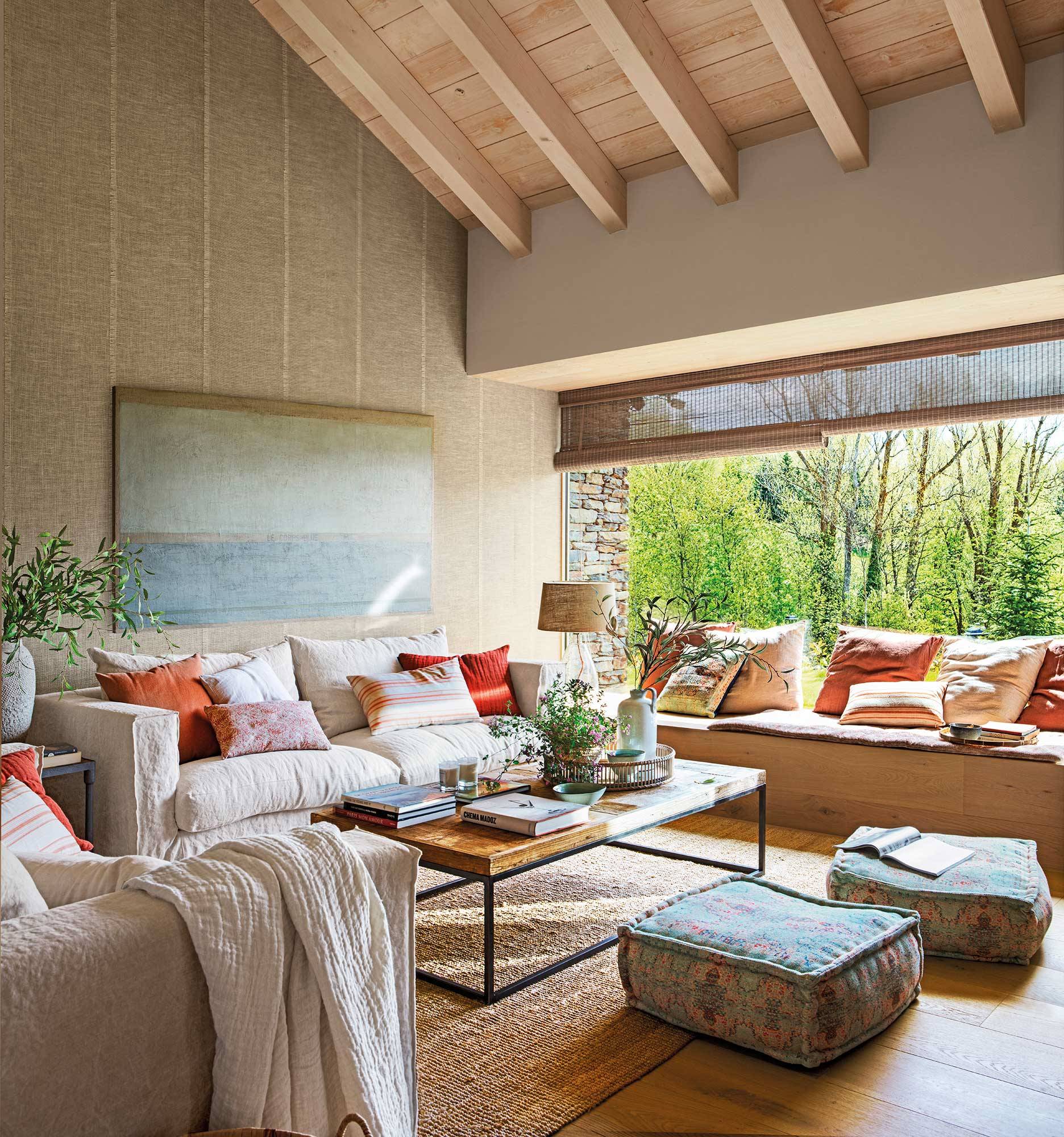 Salón rústico con grandes ventanales, alfombra de fibras y techo abuhardillado con vigas de madera.