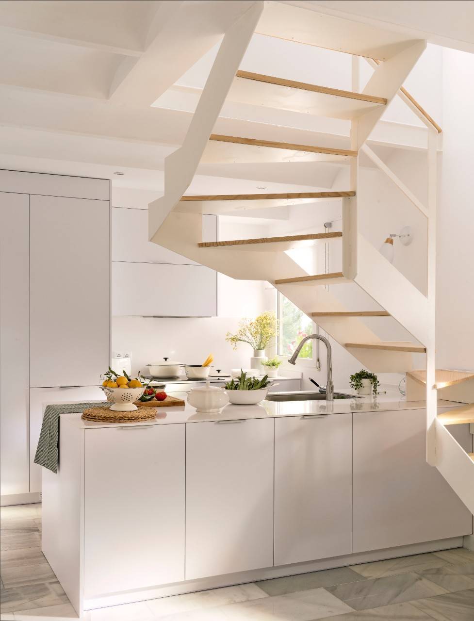 Cocina blanca bajo la escalera en piso pequeño