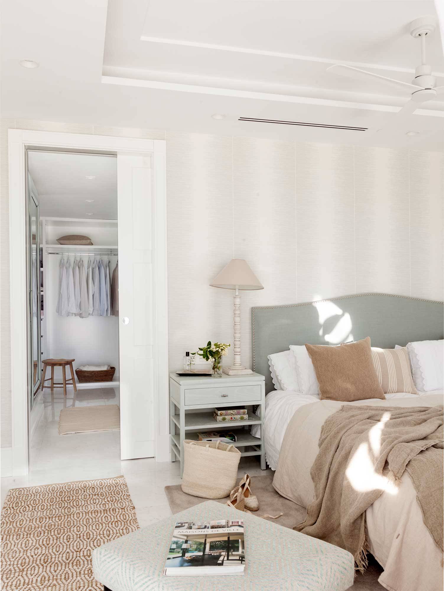 Dormitorio con pared del cabecero con papel a rayas y corredera que separa el vestidor.