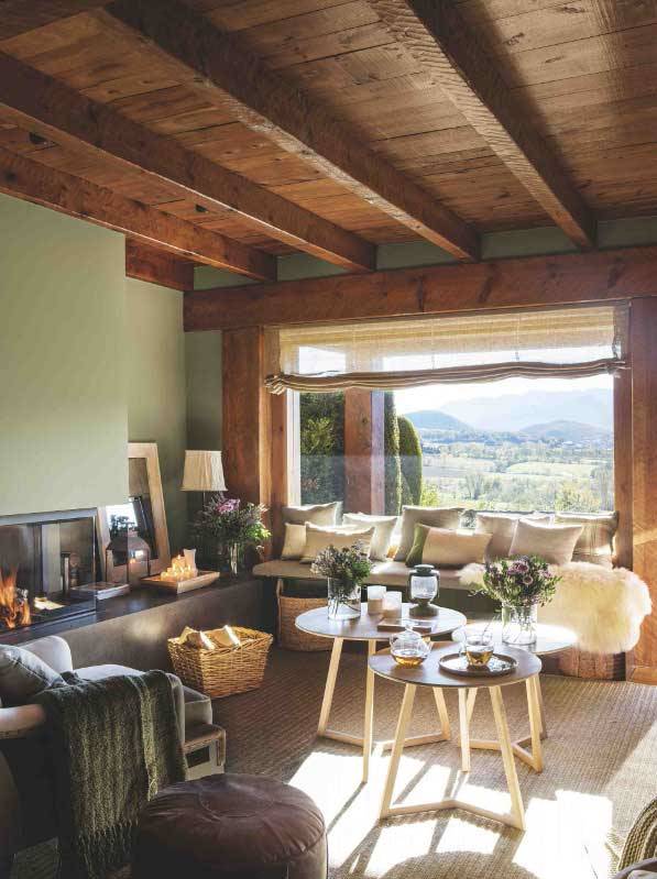 Salón de casa de montaña revestido de madera con paredes en verde y gran ventanal al jardín