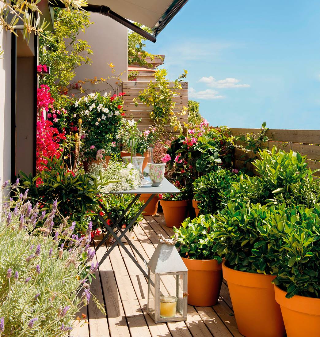 Terraza pequeña con mesa plegable de jardín de metal, macetas con plantas y farol con vela