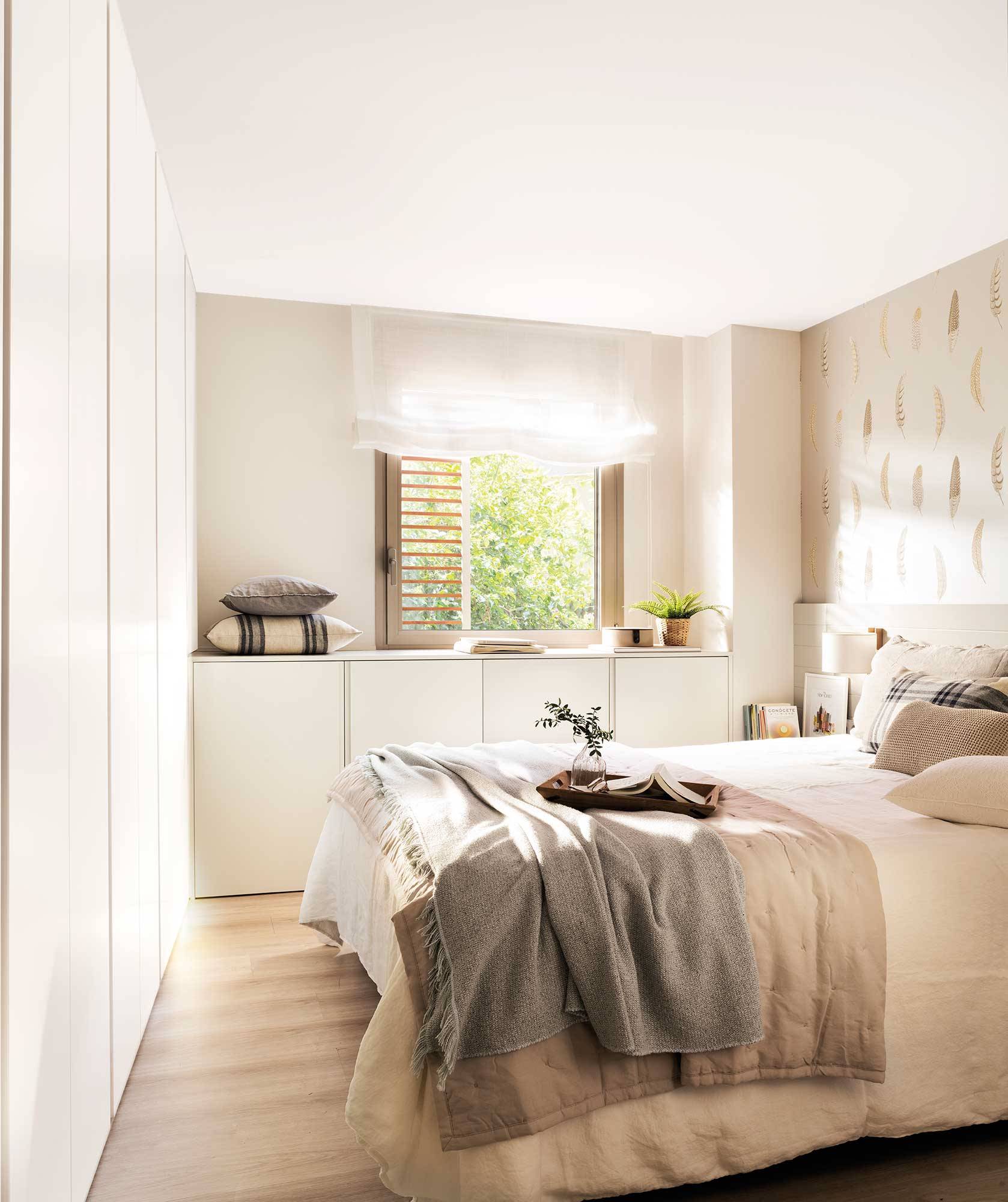 Dormitorio blanco con armarios a pie de cama y bajo la ventana_00522548