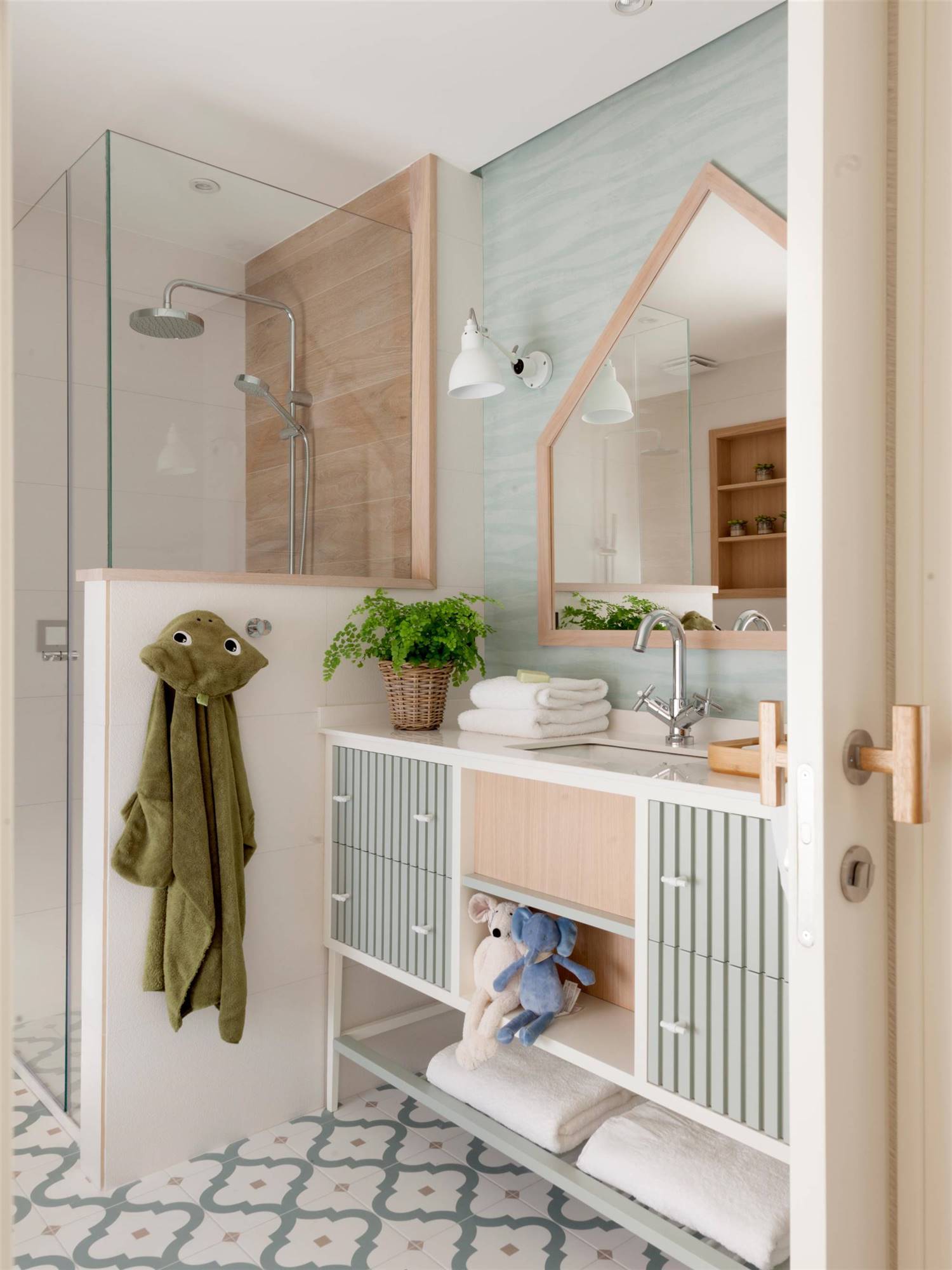 Baño infantil con espejo con forma de casita, mueble a rayas en gris y pared gris verdosa.